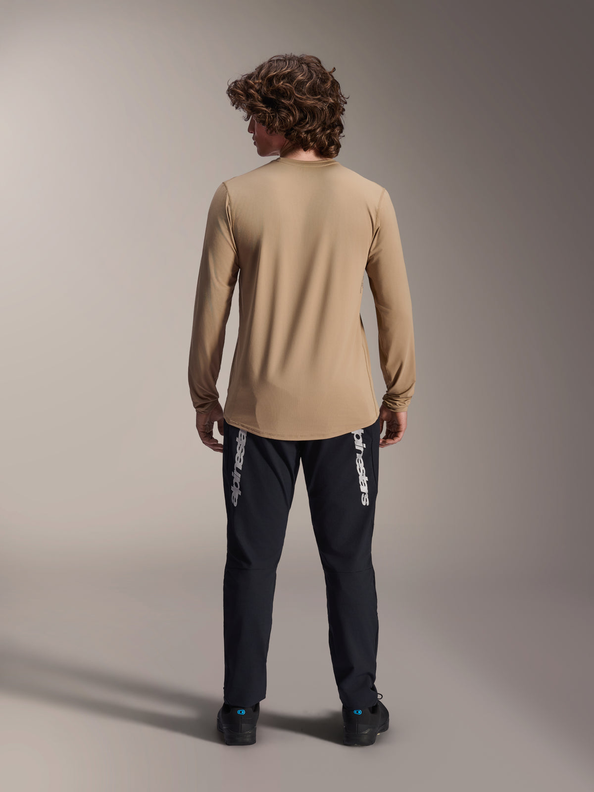 Alpinestars A-Dura Astar langærmet trøje, lysebrun, rygvisning der viser den længere drop hale, bæres med sorte bukser med Alpinestars-branding, performance mountainbike-beklædning