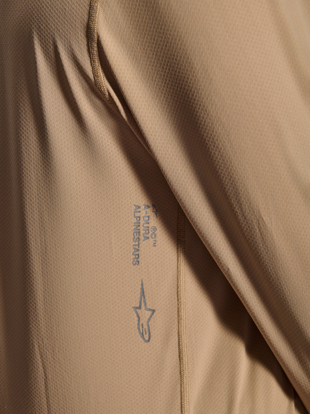 Alpinestars A-Dura Astar langærmet trøje, MTB-cykeltrøje, brun, nærbillede der viser jacquard-tekstur, printet Astars-logo og A-Dura-ordmærke, teknisk mountainbike-beklædning
