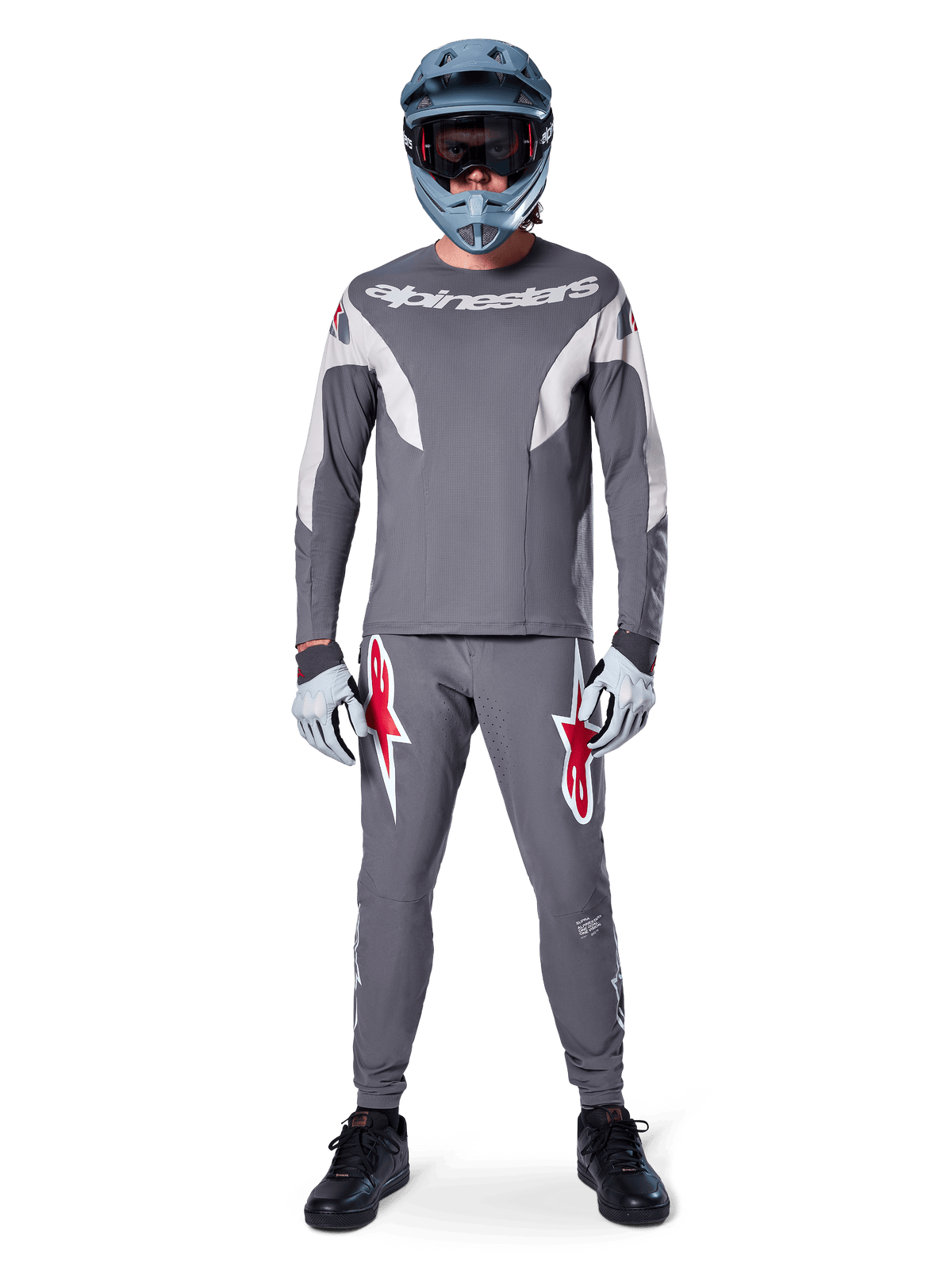 Rytter iført Alpinestars A-Supra Race Jersey - langærmet i mørkegrå, koordineret med matchende grå bukser med markante røde stjernelogoer, grå hjelm med goggles og lysegrå handsker, komplet MTB-racerudstyr til performance off-road cykling