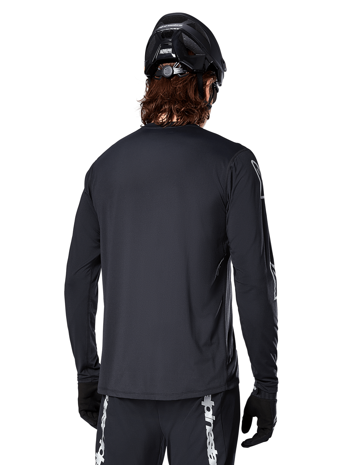 Alpinestars A-Dura Switch langærmet trøje, sort, set bagfra på en cyklist iført sort MTB-hjelm og handsker, teknisk jacquard-stof og forlænget ryg til terrænkørsel