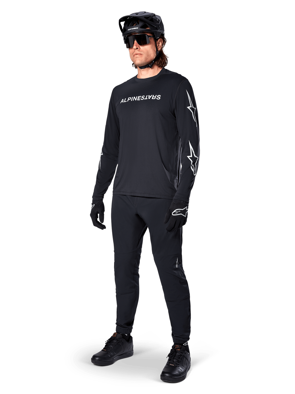 Alpinestars A-Dura Switch langærmet trøje, sort, mountainbike-trøje båret med sorte bukser, hjelm og handsker, med hvidt ordmærke-logo på brystet og stjernelogoer på ærmerne, koordineret MTB-udstyr til terrænkørsel