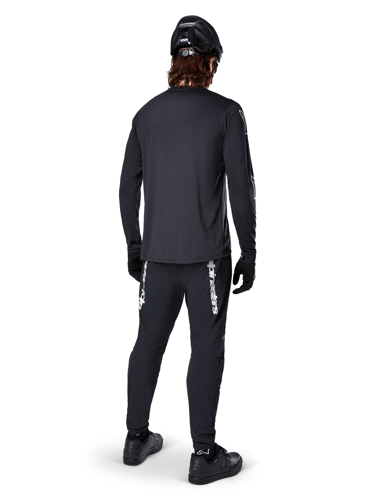 Alpinestars A-Dura Switch langærmet trøje, sort, set bagfra på en rytter, båret med sorte bukser med hvidt Alpinestars-branding, sort hjelm og handsker, med længere drop tail for ekstra dækning, performance mountainbike-beklædning