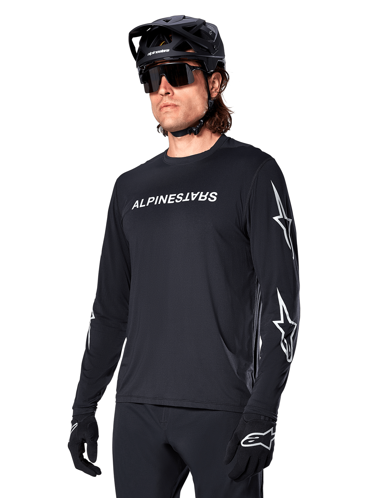 Mandlig cyklist iført Alpinestars A-Dura Switch langærmet trøje, sort med hvidt ordmærke og stjernelogoer på ærmerne, stylet med sort MTB-hjelm og solbriller, højtydende cykeludstyr til terrænkørsel