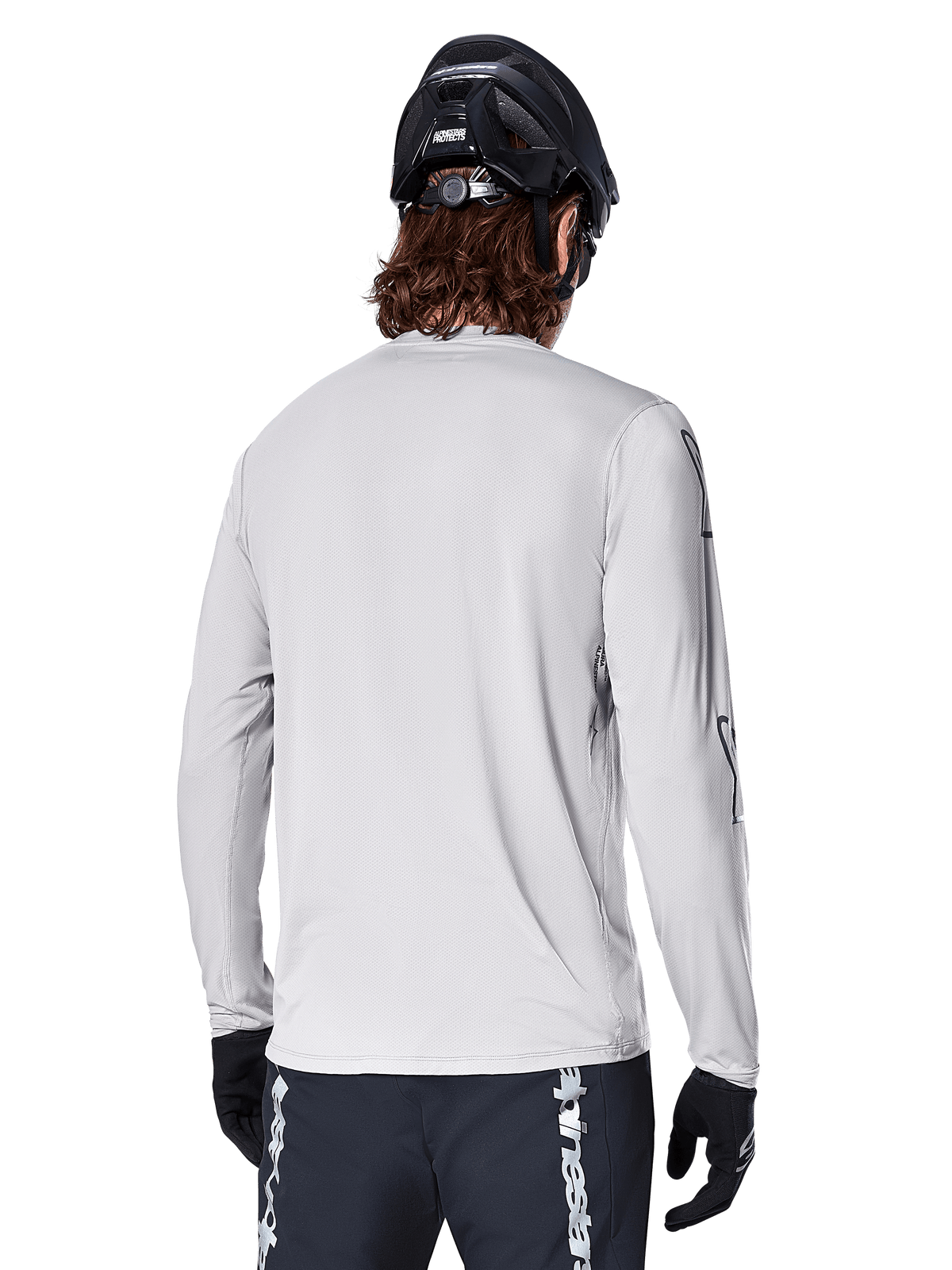 Alpinestars A-Dura Switch langærmet trøje, lysegrå, set bagfra af en mountainbiker iført sort MTB-hjelm og handsker, med længere bagstykke for ekstra dækning og tekstureret jacquard-stof, performance cykeludstyr