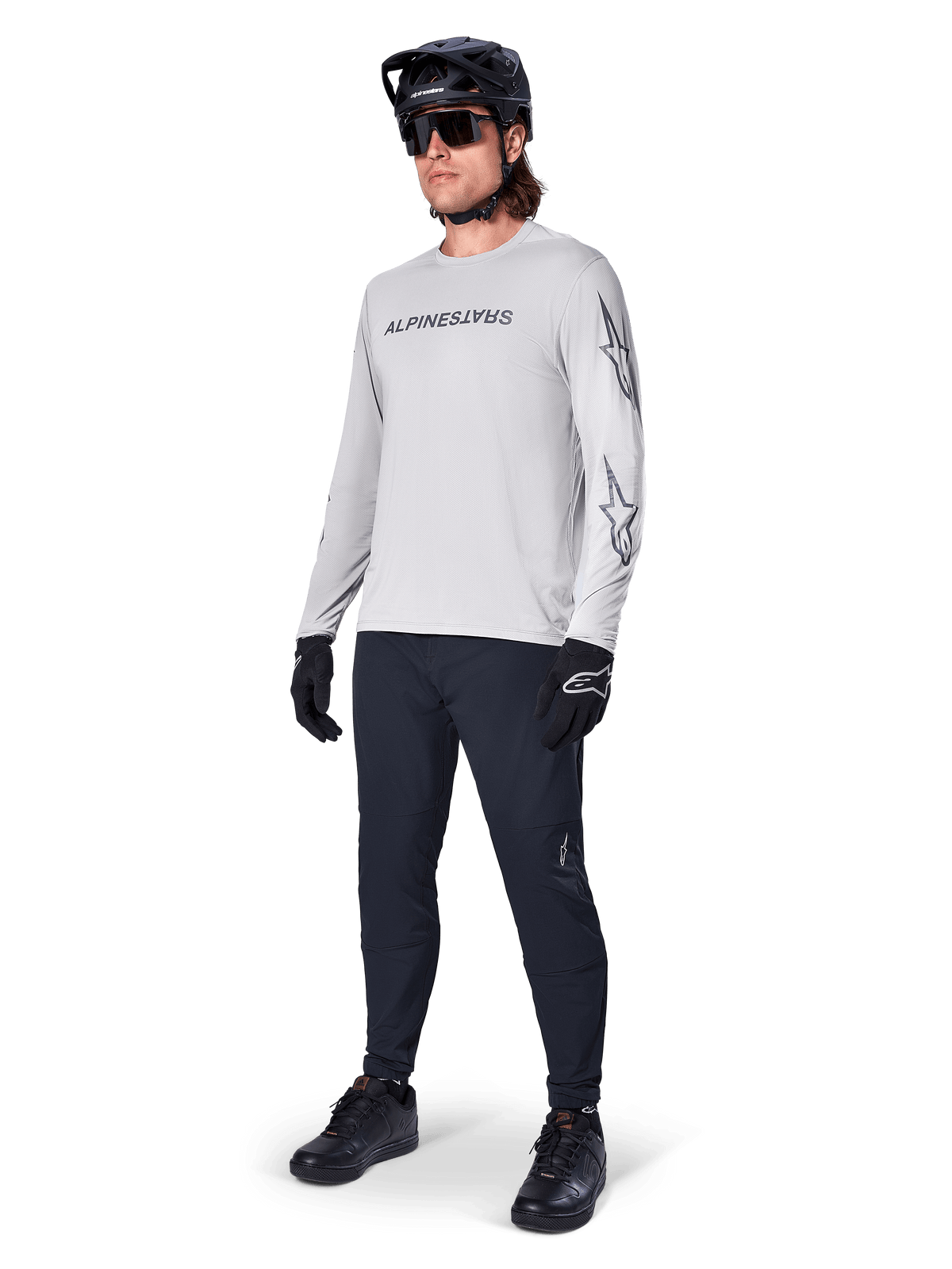 Alpinestars A-Dura Switch langærmet trøje, lysegrå, båret af mandlig rytter med sorte mountainbike-bukser og hjelm, med sort logo på brystet og stjernegrafik på ærmerne, performance mountainbike-udstyr