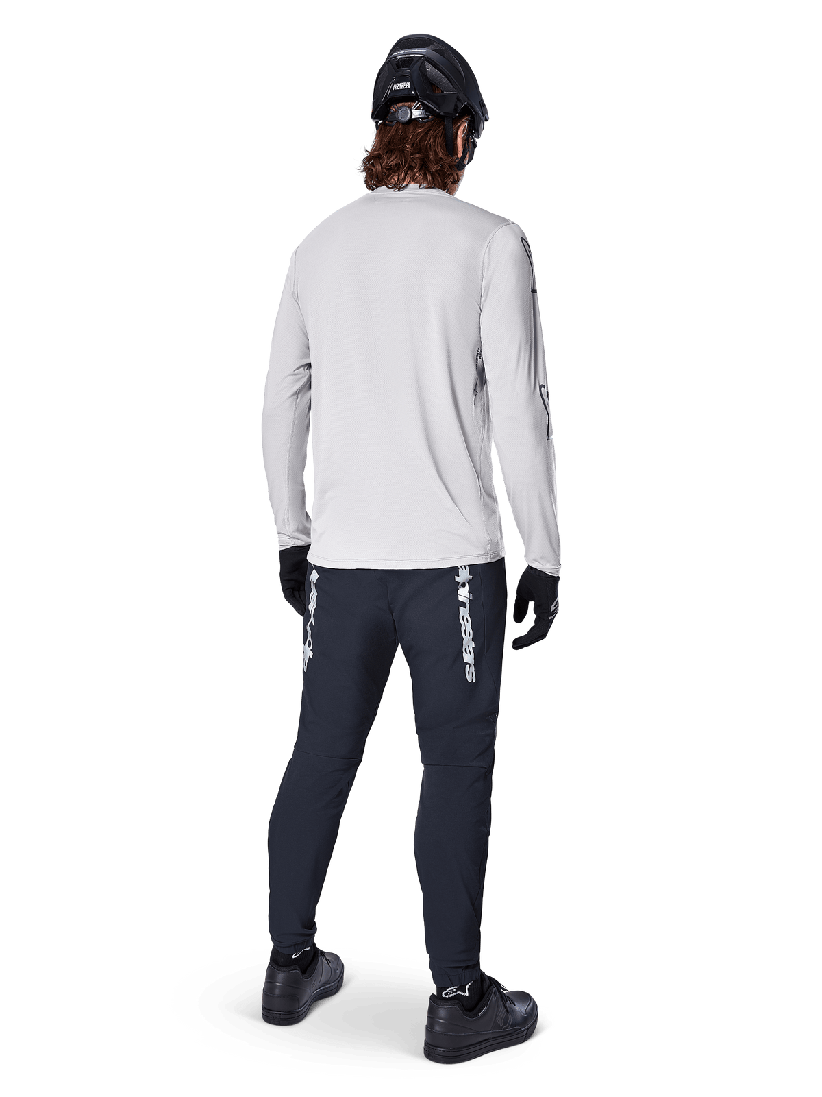 Alpinestars A-Dura Switch langærmet trøje, lysegrå, set bagfra på en rytter iført sorte cykelbukser, hjelm og handsker, højtydende mountainbike-udstyr med en længere drop tail.