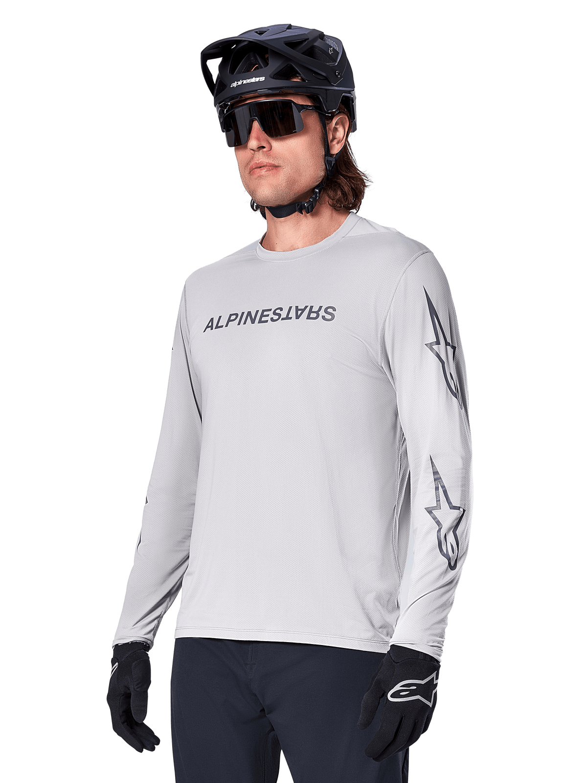 Alpinestars A-Dura Switch langærmet jersey, mountainbike jersey, lysegrå, sort wordmark-skærmprint på brystet og stjernelogoer på ærmerne, bæres med sort mountainbikehjelm, mørke solbriller og sorte handsker, atletisk terrængående cykeludstyr