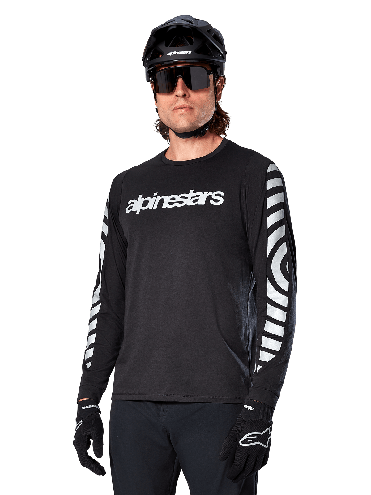 Alpinestars A-Dura Dri Oscar Long Sleeve Jersey, MTB Cycling Jersey, Black Reflective, featuring a white chest wordmark and bold reflective circular graphics on the sleeves, worn with a black helmet and sunglasses, technical moisture-wicking apparel for off-road mountain biking