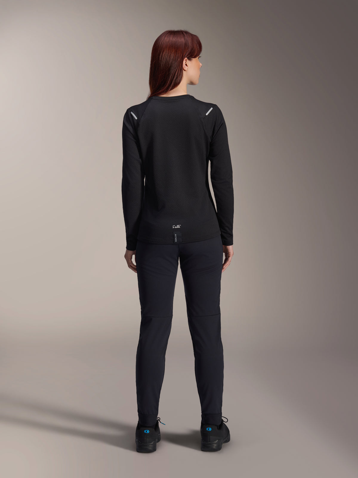 Alpinestars Stella A-Dura Thermal trøje til kvinder, set bagfra, sort, langærmet cykeltrøje med isolerende fleece, kombineret med matchende sorte bukser og sko, med diskret A-Dura-branding nederst på ryggen og reflekterende detaljer på skuldrene, skræddersyet til MTB-kørsel til kvinder.