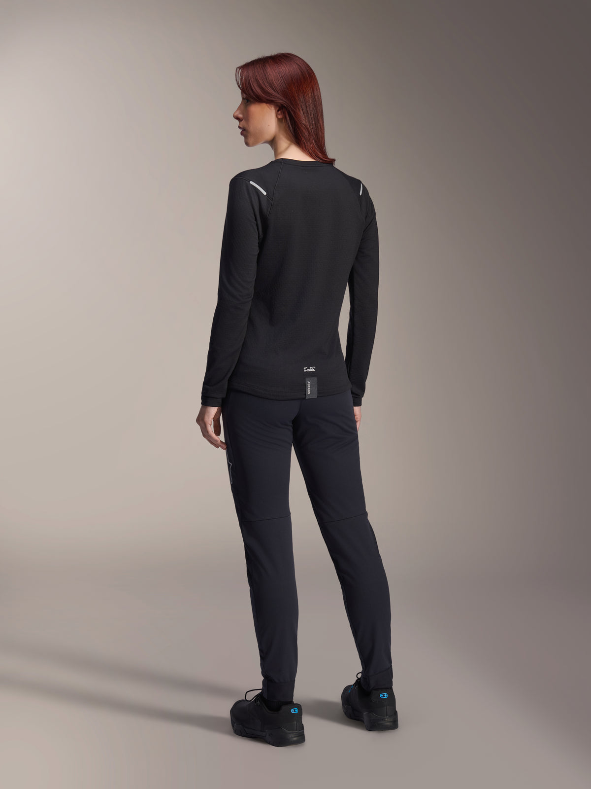 Alpinestars Stella A-Dura Thermal trøje til kvinder, langærmet MTB-trøje i sort, set bagfra med reflekterende skulderdetaljer og forlænget drop tail, kombineret med sorte bukser og sko, performance-udstyr til mountainbike.