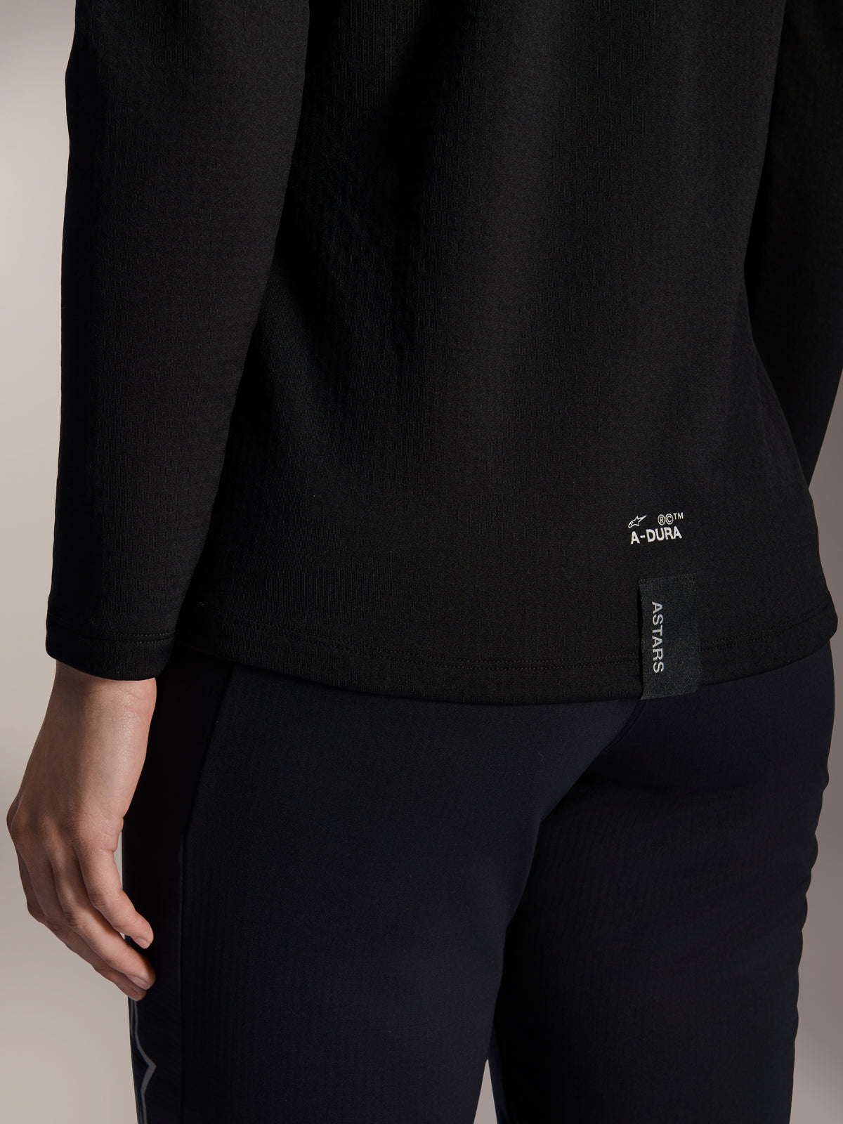 Alpinestars Stella A-Dura termotrøje til kvinder, sort MTB-termotrøje, nærbillede af den nederste kant bagpå med hvidt A-DURA-branding og lodret ASTARS-logotag, designet til mountainbike i koldt vejr