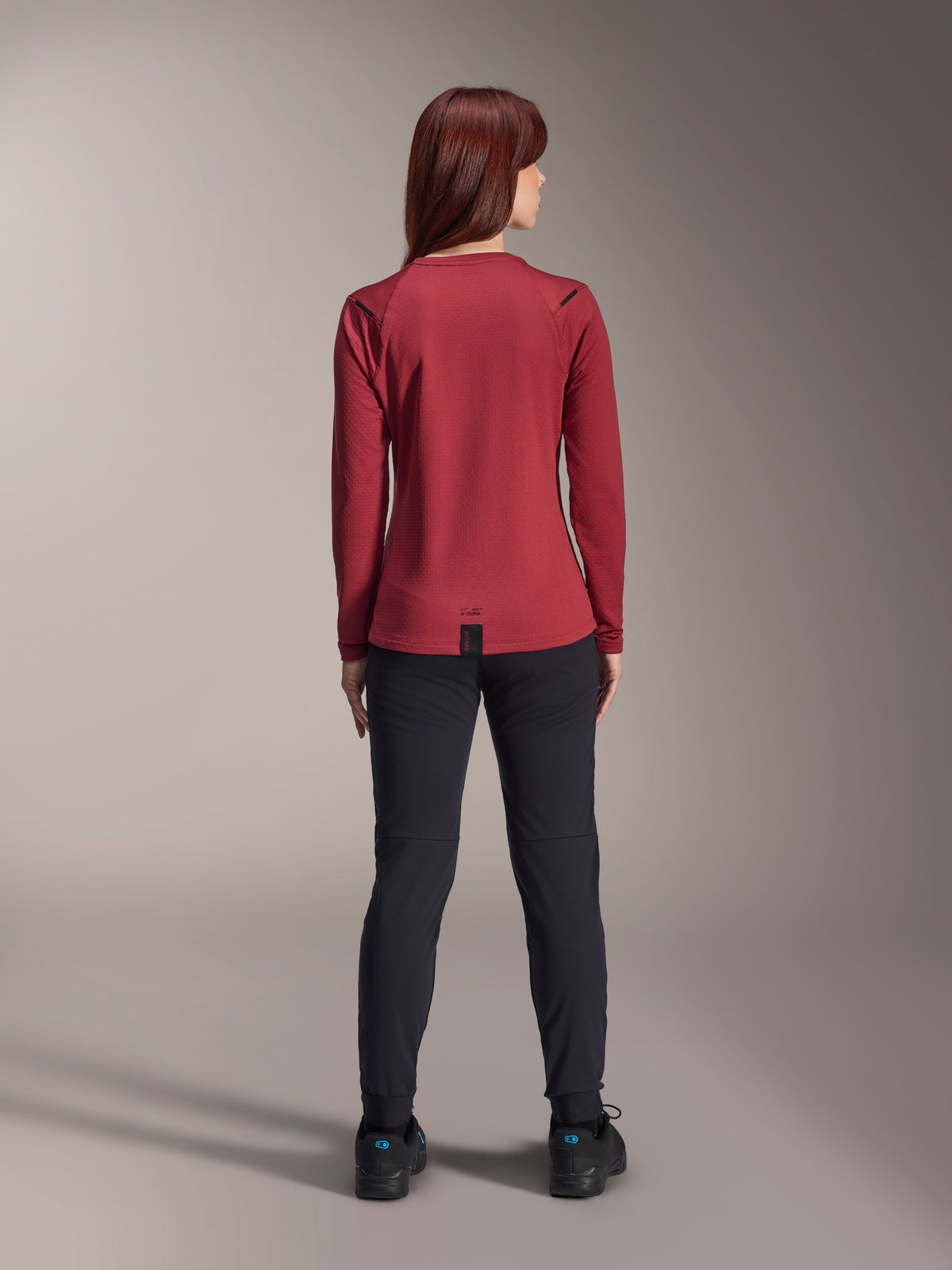 Alpinestars Stella A-Dura Thermal Jersey til kvinder, vinrød, set bagfra, langærmet isoleret cykeltrøje med forlænget ryg, kombineret med sorte bukser og sorte cykelsko, mountainbike-beklædning