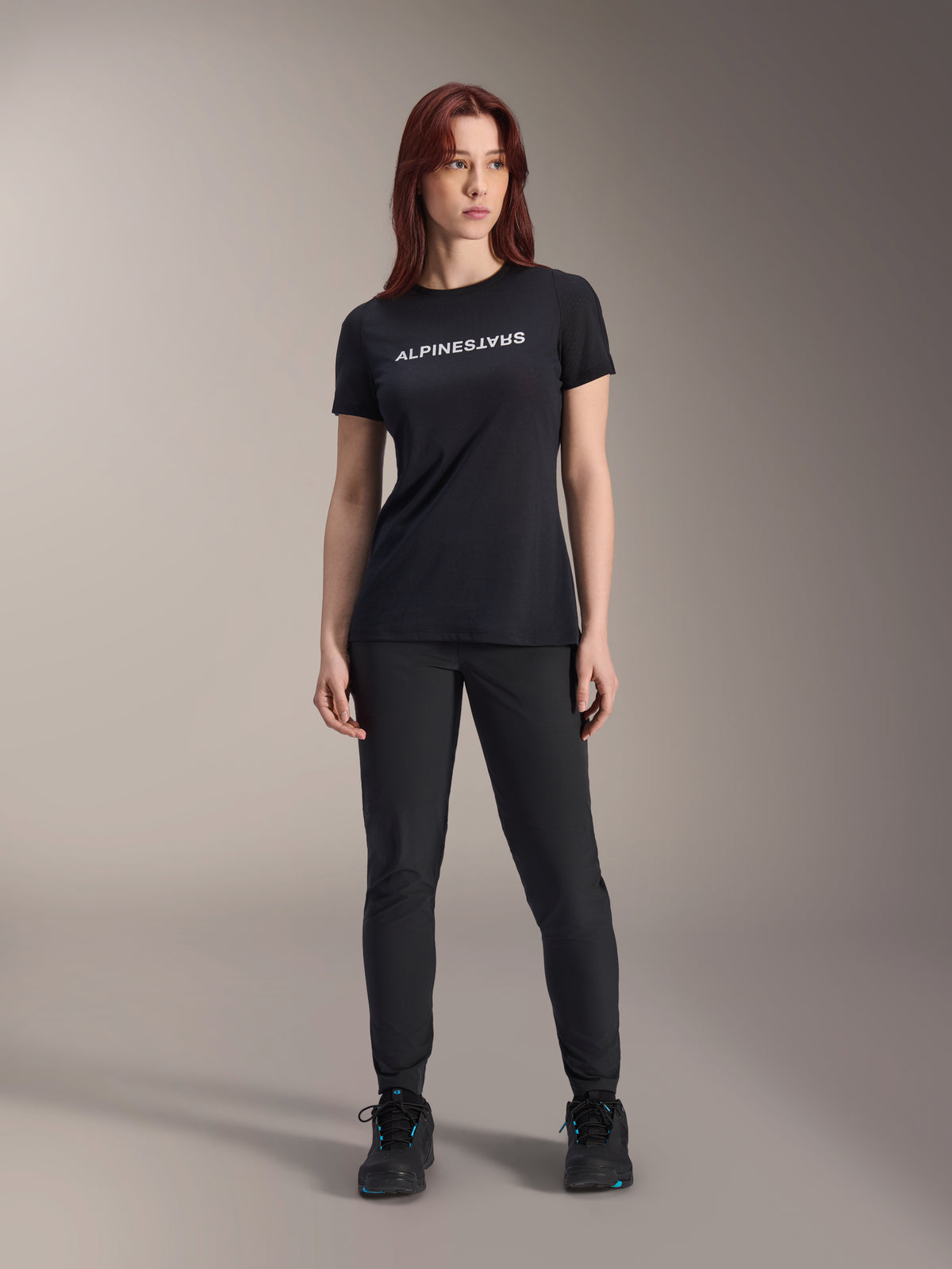 Model wearing Alpinestars Women Stella A-Dura Dri Switch Short Sleeve Jersey in Black, featuring white logo branding on the chest, paired with black technical pants and black athletic shoes, full-body studio shot
