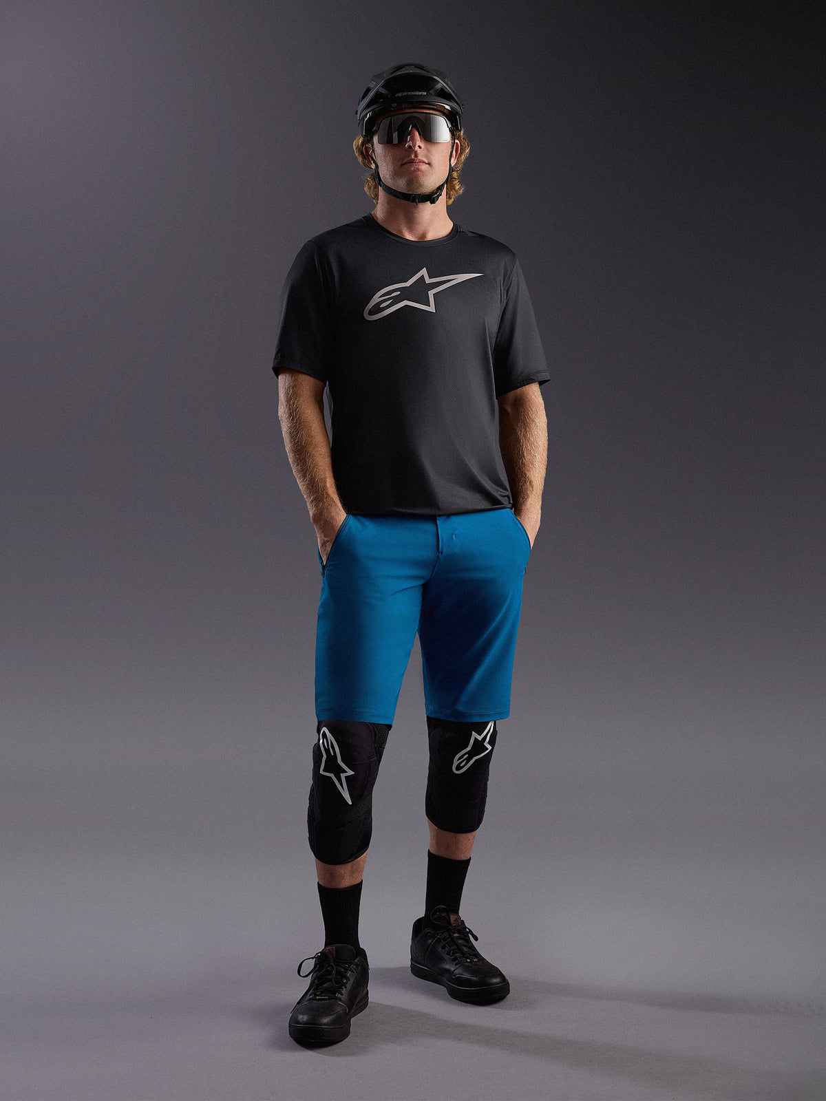 Alpinestars A-Dura Ride SS trøje og blå shorts, komplet mountainbike-outfit med beskyttelsesudstyr og hjelm.
