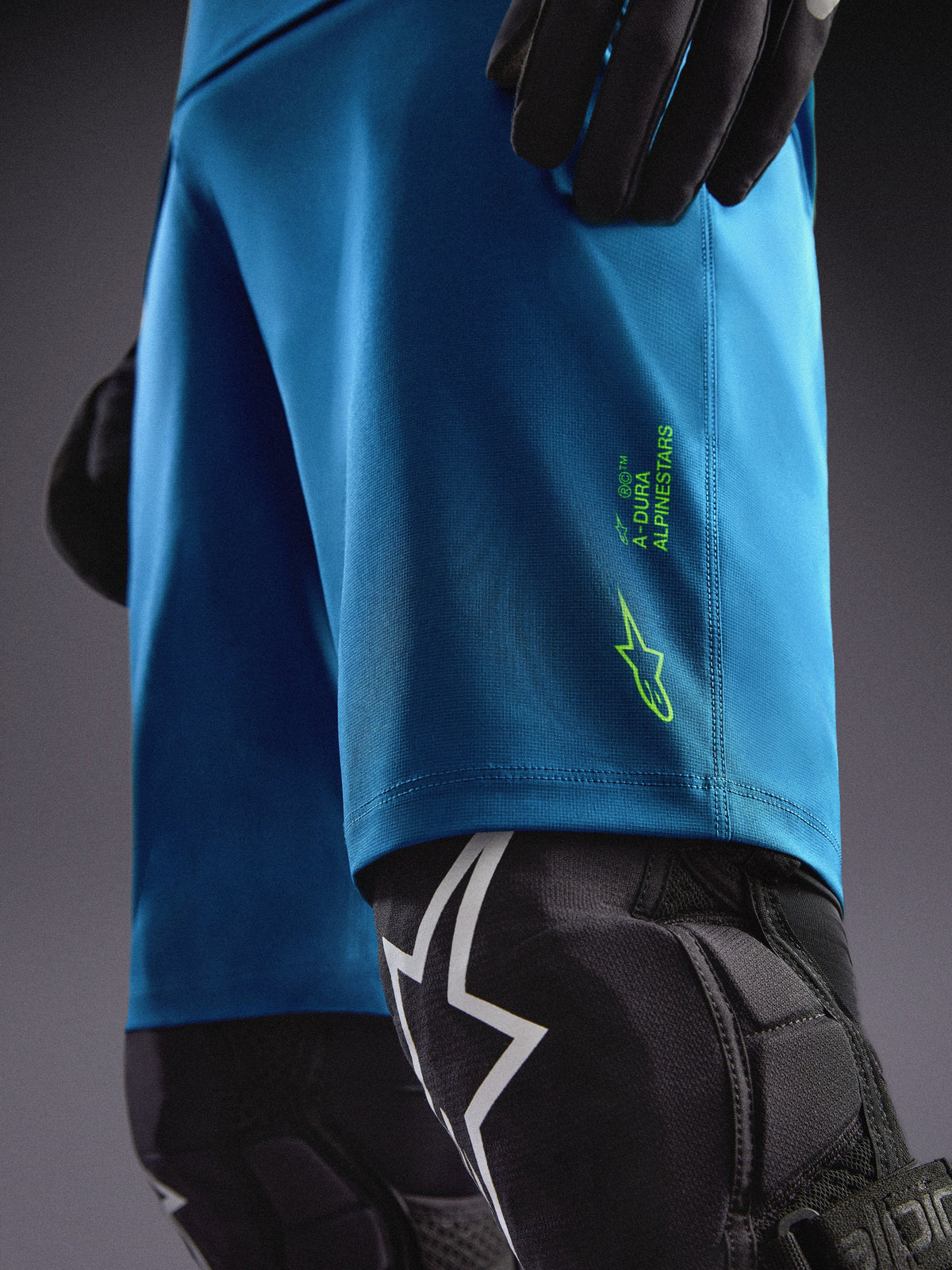 Alpinestars A-Dura Ride Shorts i blågrøn med limegrønne logoer, parret med knæbeskyttere til MTB-kørsel.