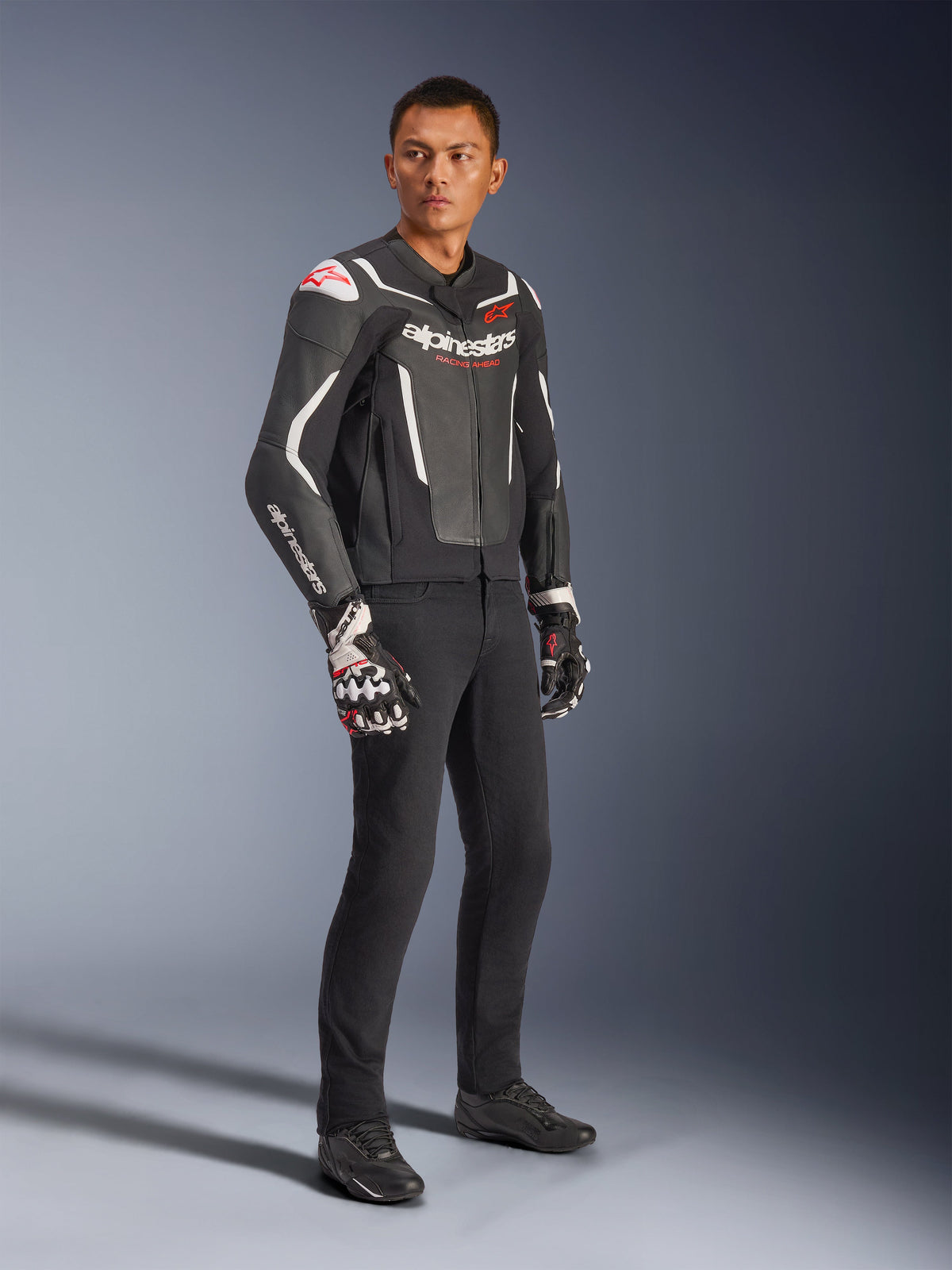 Alpinestars GP Force V2 læderjakke, sort og hvid, båret af mandlig model med sorte kørebukser og tekniske handsker, med røde Alpinestars-logoer, sport-fit læder motorcykeljakke til landevejskørsel