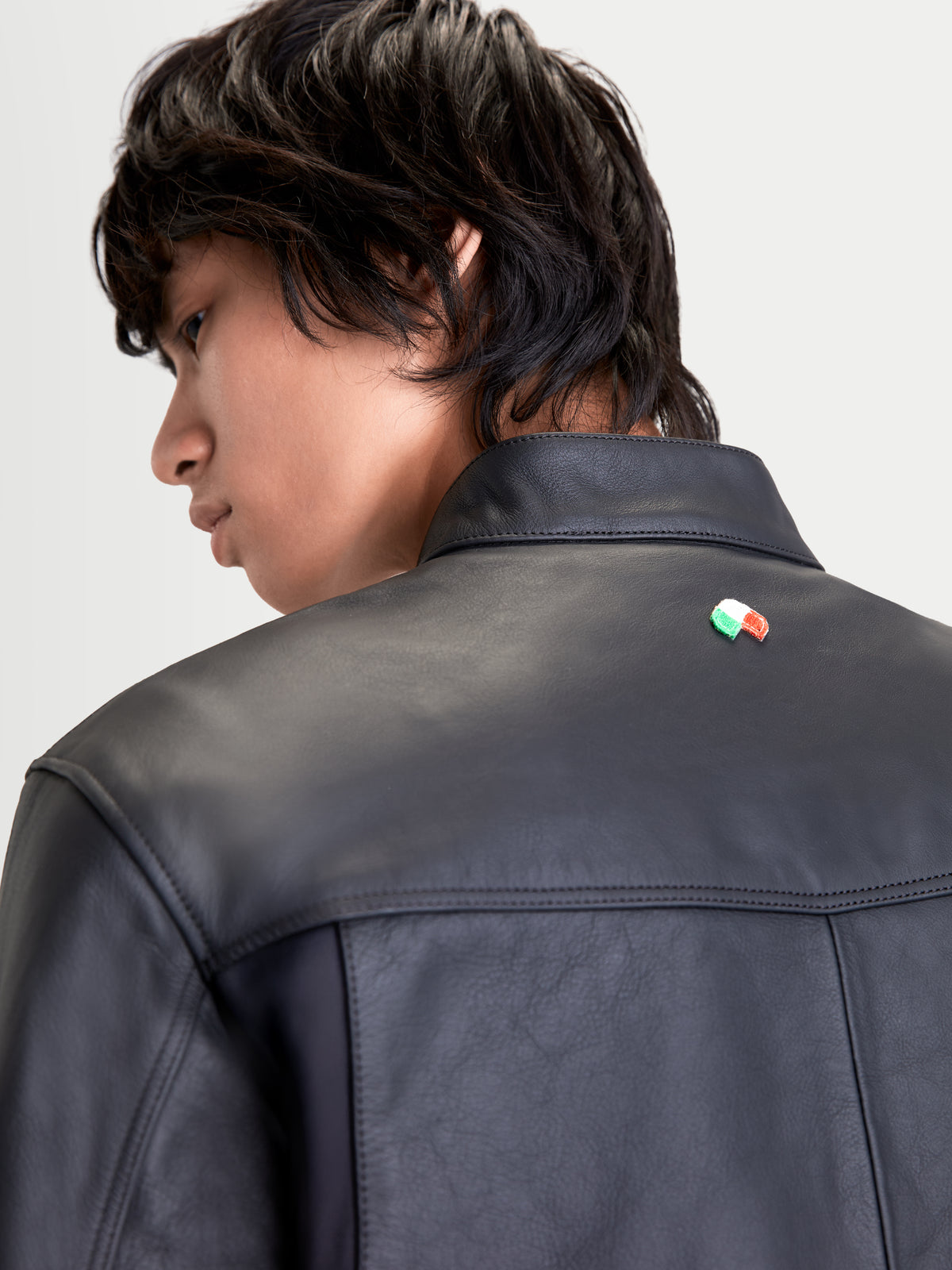 Alpinestars Maver-X Leather Jacket, men's urban motorcycle leather jacket in black, close-up back view showing premium bovine leather construction, biker collar, and Italian flag detail worn by a model