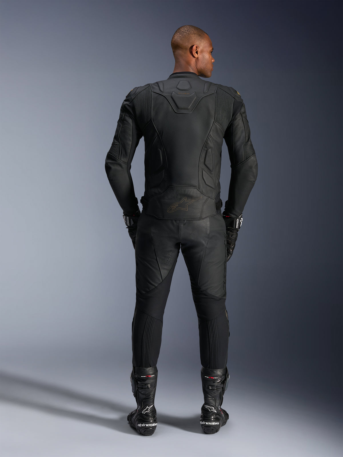 Alpinestars Dusk læderjakke, sort motorcykelracingjakke i bovint læder, set bagfra på en kører i beskyttelsesudstyr.