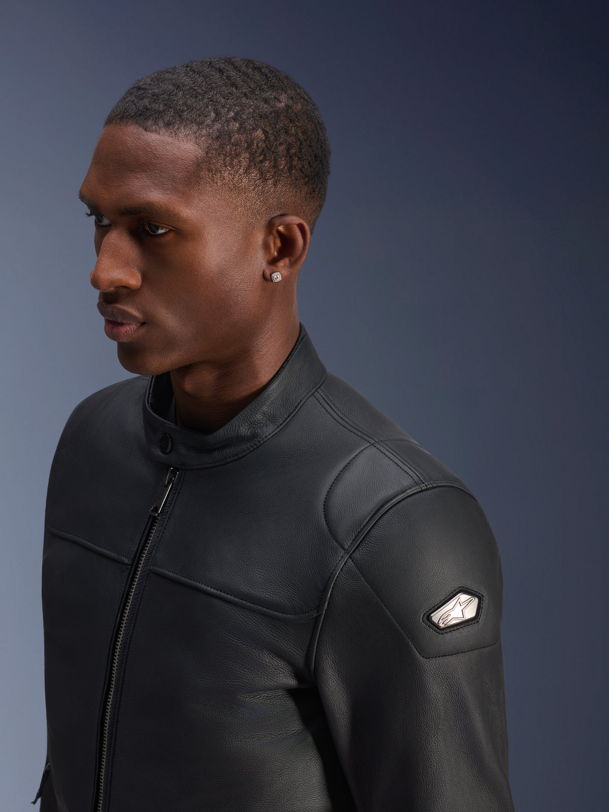Alpinestars Blacktrack læderjakke, urban motorcykeljakke til herrer i sort bovint læder med metallisk skuldermærke og gunmetal lynlås.