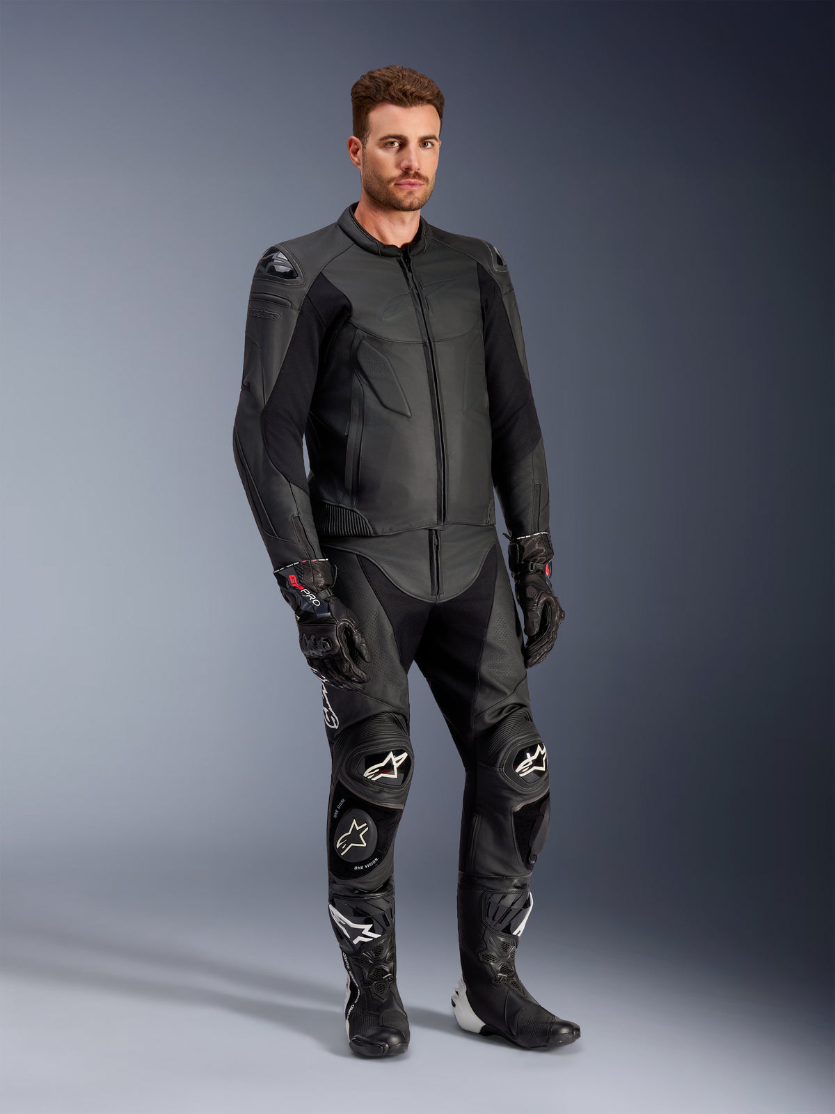 Mandlig model iført Alpinestars Caliber læderjakke i sort, kombineret med matchende sorte lædermotorcykelbukser, racinghandsker og støvler, som viser et komplet sportsligt motorcykeloutfit til vej.