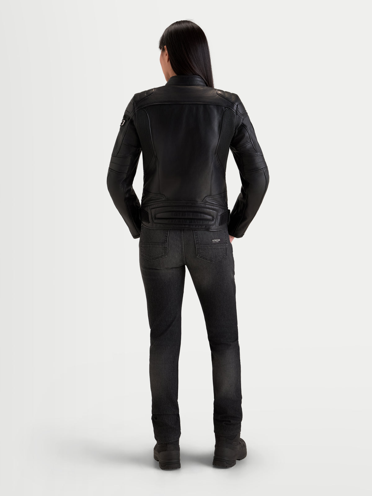 Alpinestars Revea Kvinde Læderjakke, urban dame-motorcykellæderjakke i sort, set bagfra på en model iført mørke jeans og køresko, fuldnarvet okselæderkonstruktion