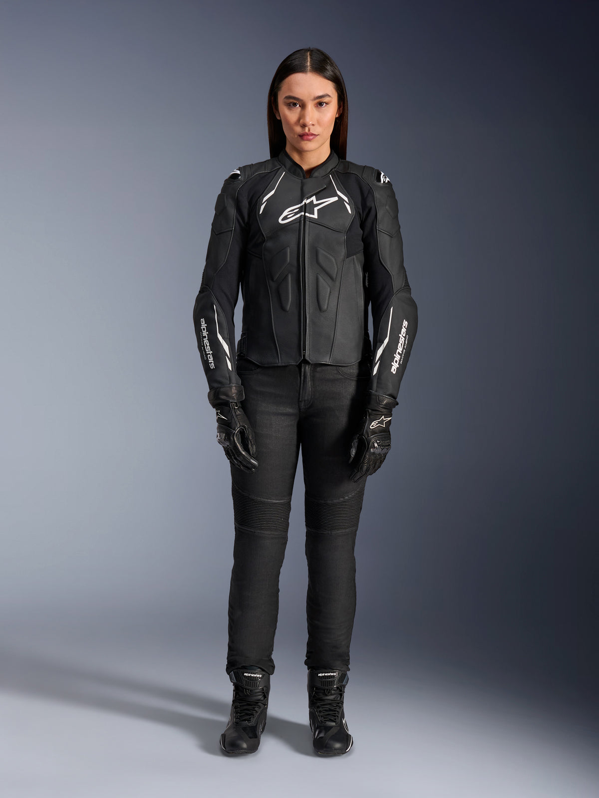 Alpinestars Stella Dusk læderjakke til kvinder, sort og hvid, båret af en model med matchende sorte bukser og støvler, set forfra, med hvide Alpinestars-logoer på brystet og ærmerne, beskyttelsesudstyr i premium okselæder til kvinder