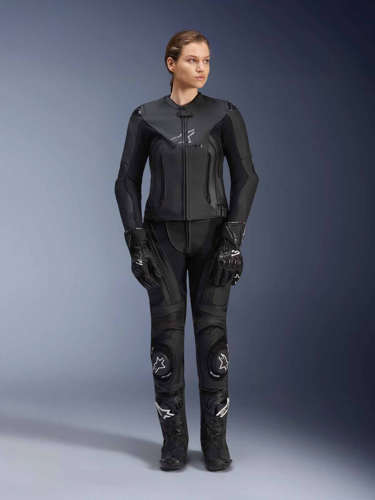 Alpinestars Stella GP Plus V4 læderjakke til kvinder i Sort Sort, båret af en kvindelig kører med matchende læder-racerbukser, handsker og støvler, med en skræddersyet pasform, central lynlås og diskret branding på brystet, koordineret til sport- og landevejskørsel på motorcykel.