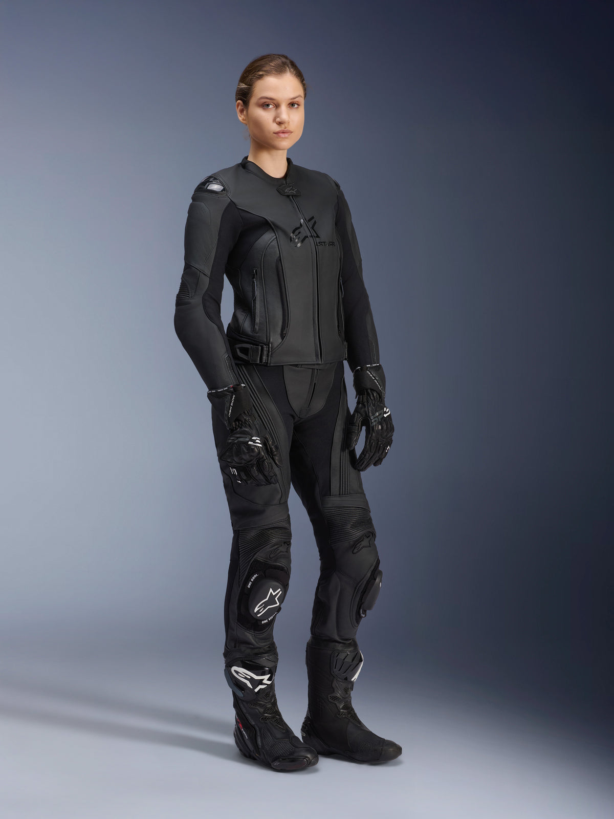 Kvindelig motorcyklist iført Alpinestars Stella GP Plus V4 læderjakke til kvinder i sort, stylet som en komplet racerdragt i læder med matchende motorcykelbukser, handsker og støvler, med et strømlinet præstationsdesign med integreret beskyttelse.
