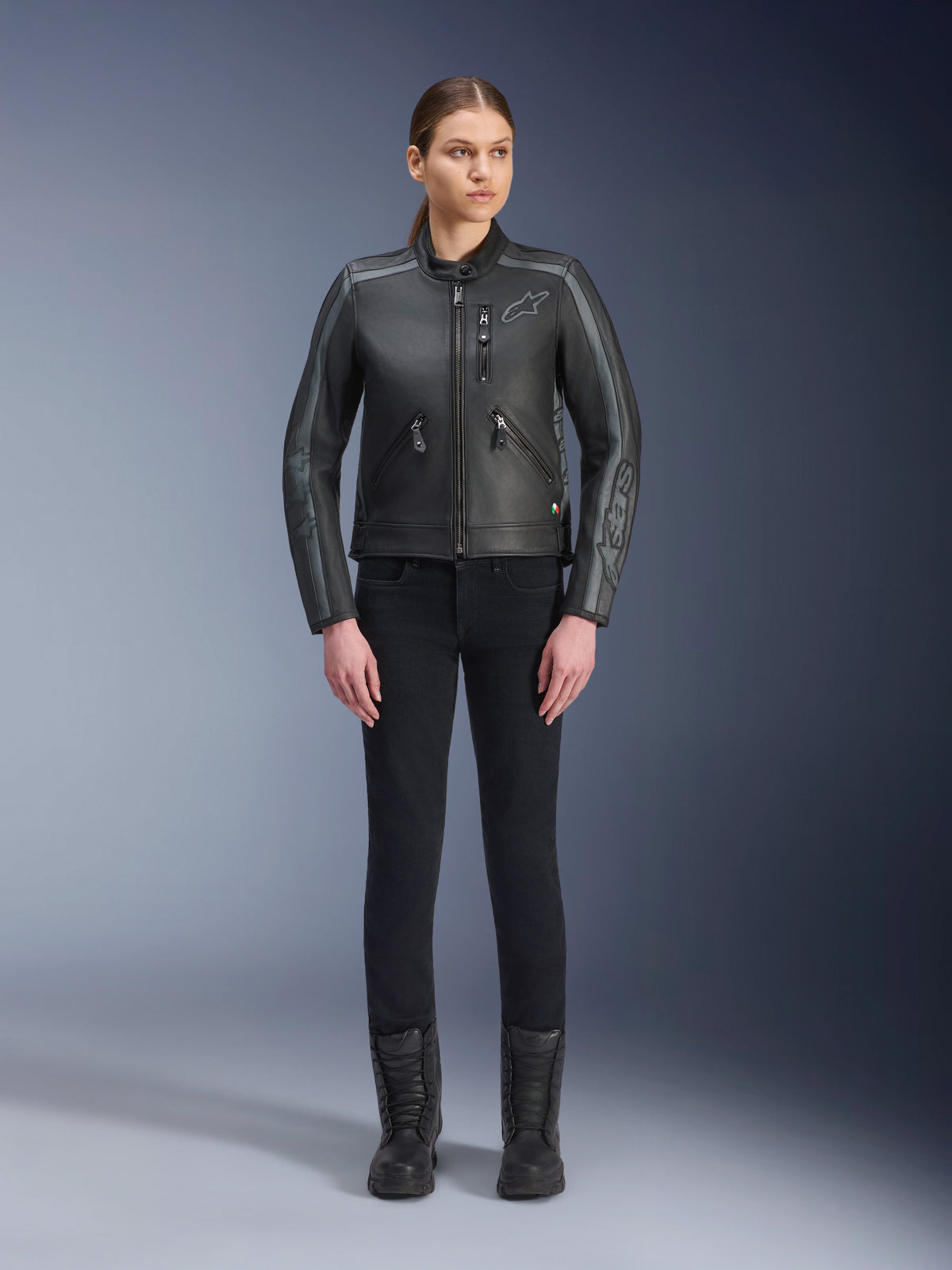 Alpinestars Stella Dyno læderjakke, motorcykeljakke til damer, Black Tar Gray Dark Gray, fuld kropsvisning i studie af en model iført jakken med sorte slim-fit bukser og sorte støvler, konstruktion i okselæder med grå detaljer og diskret Alpinestars-branding på bryst og ærmer.
