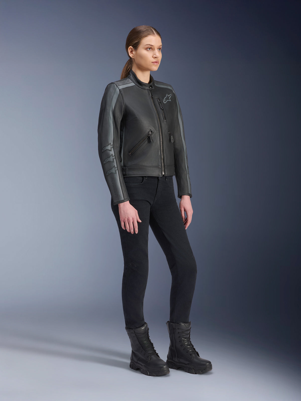 Alpinestars Stella Dyno læderjakke, motorcykeljakke til kvinder, Black Tar Gray og Dark Gray, båret med sorte bukser og støvler, med grå racerstriber på ærmerne og heritage læderdesign