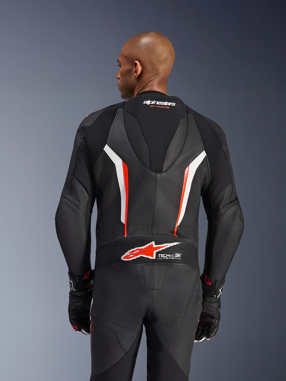 Alpinestars GP Force V2 læderdragt, 1-delt motorcykeldragt, sort, hvid og fluorescerende rød, overkrop set bagfra med perforeret læder og Tech-Air Ready-logo, båret med matchende sorte og røde handsker
