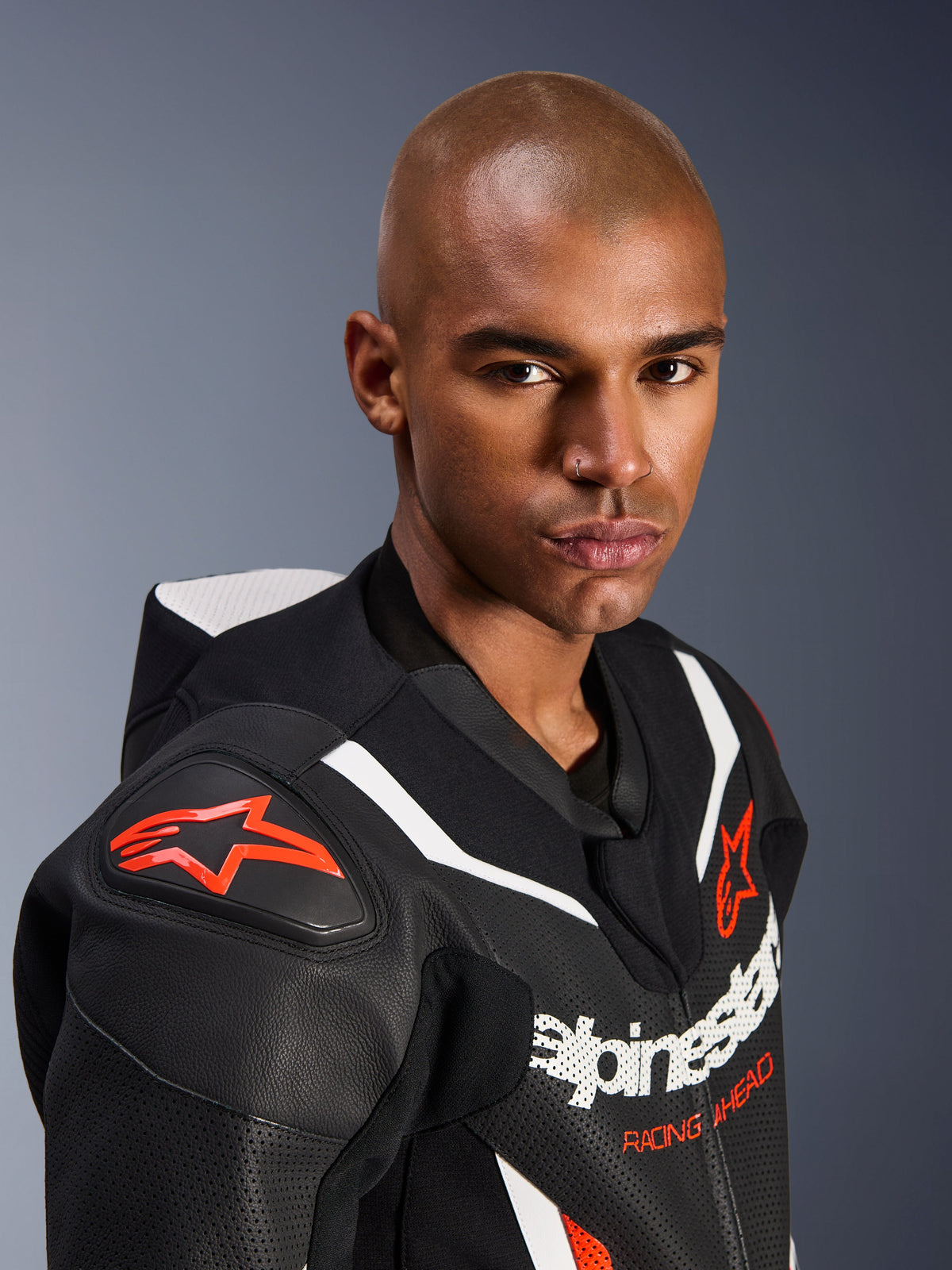 Nærbillede af en model iført Alpinestars GP Force V2 læderdragt, 1-delt, sort, hvid og rød fluo, med perforerede læderpaneler, hvide racerstriber og røde Alpinestars-logoer på skulder og bryst.