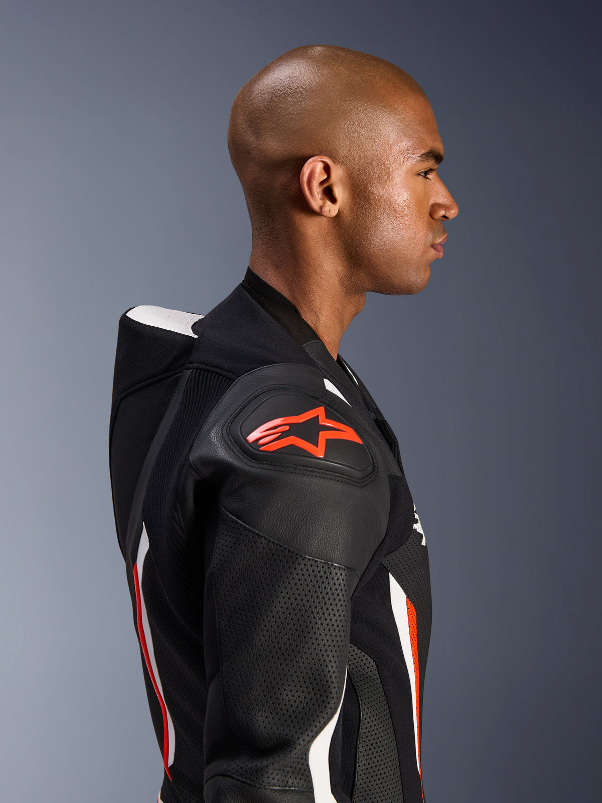 Alpinestars GP Force V2 læderdragt - 1Piece, sideprofil af en kører, Black White Red Fluo farvekombination, der fremhæver den aerodynamiske speed hump, perforerede læderzoner og DFS Lite skulderbeskyttelse med rødt Alpinestars logo