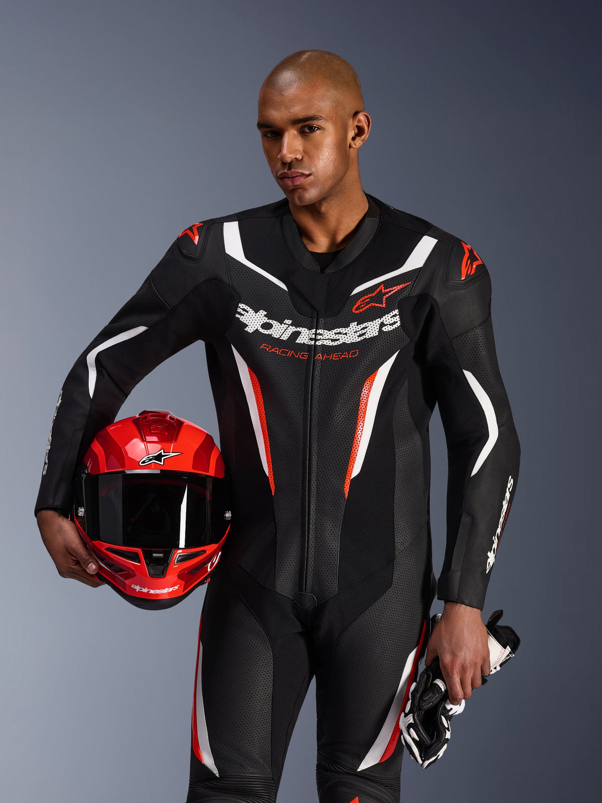 Alpinestars GP Force V2 læderdragt, 1-delet motorcykeldragt, sort, hvid og rød fluo, bæres af en model, der holder en rød hjelm og handsker, strømlinet racerdesign med perforeret læder og markant branding