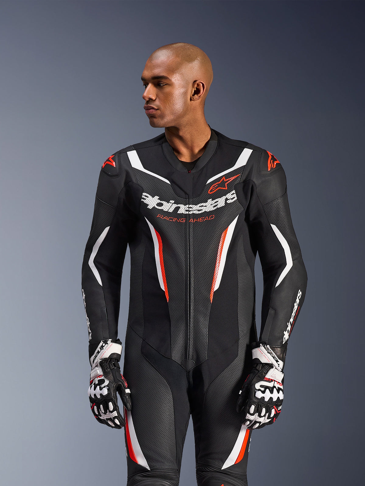 Alpinestars GP Force V2 læderdragt, 1-delt, sort, hvid og rød fluo, bæres af en mandlig model med racerhandsker, perforeret læderkonstruktion, markante hvide og røde grafiske detaljer, Alpinestars-logo på brystet