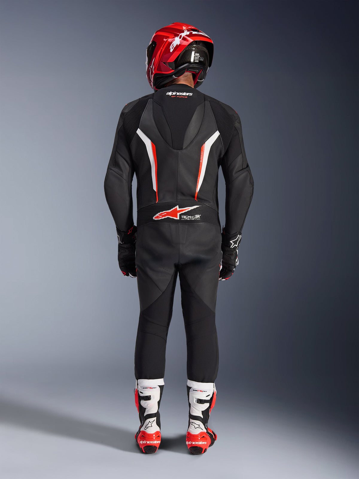 Kører set bagfra iført Alpinestars GP Force V2 læderdragt i ét stykke i sort, hvid og fluorescerende rød, med aerodynamisk speed hump og Tech-Air Ready-branding, koordineret med en rød racerhjelm og hvide og røde støvler, professionelt banekørselsudstyr.