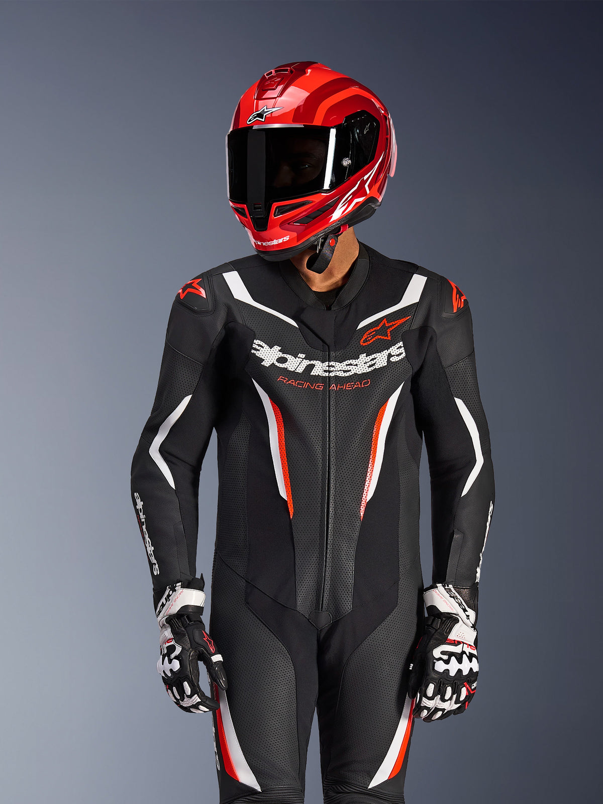 Motorcyklist iført Alpinestars GP Force V2 læderdragt i ét stykke i Black White Red Fluo, matchende rød racerhjelm og handsker, med perforerede læderpaneler og markant branding, højtydende racerudstyr