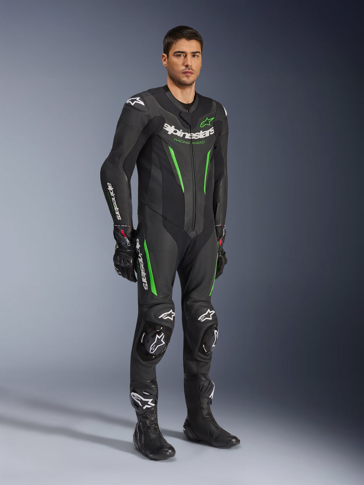 Alpinestars GP Force V2 læderdragt - 1Piece, sort og grøn, komplet racerudstyr båret med sorte handsker og støvler, med perforerede læderpaneler, hvid Alpinestars-branding og integrerede knæslidere, professionel dragt til banekørsel