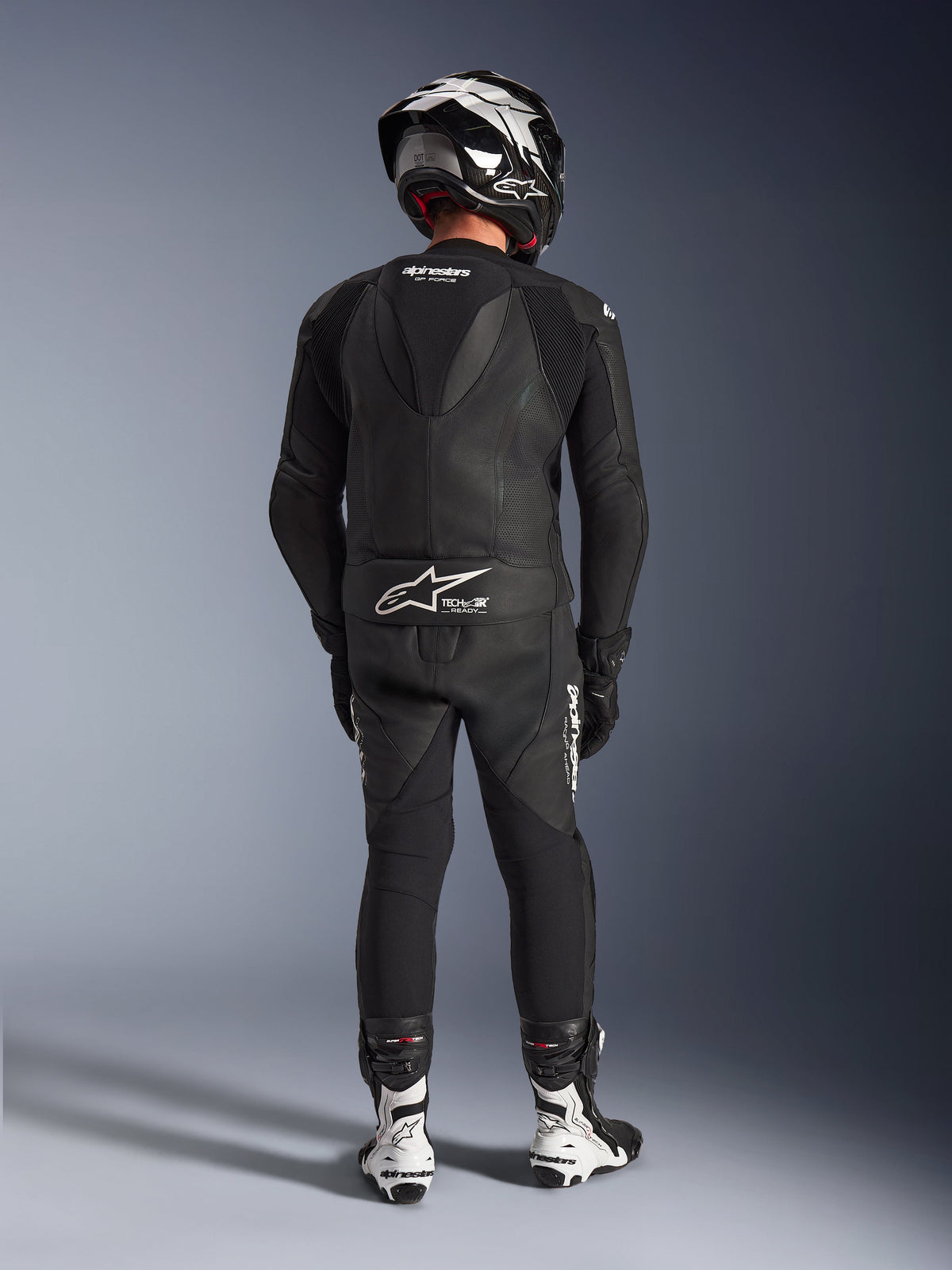 Alpinestars GP Force V2 2-Piece Leather Suit in Black, full rear view showing aerodynamic speed hump and Tech-Air Ready branding, paired with matching black and white helmet and white racing boots for professional track performance
