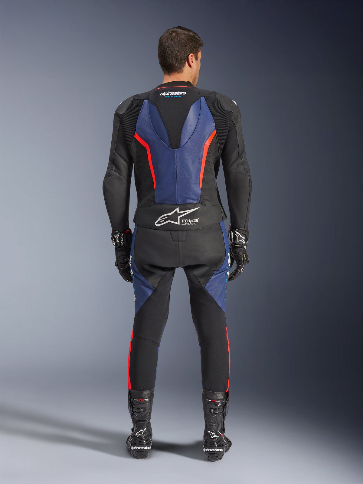 Alpinestars GP Force V2 2-delt læderdragt, set bagfra, sort, blå og rød fluo, med blå læderpaneler på ryggen og benene med neonrøde detaljer, Tech-Air Ready-branding på lænden, vist med sorte racinghandsker og støvler.