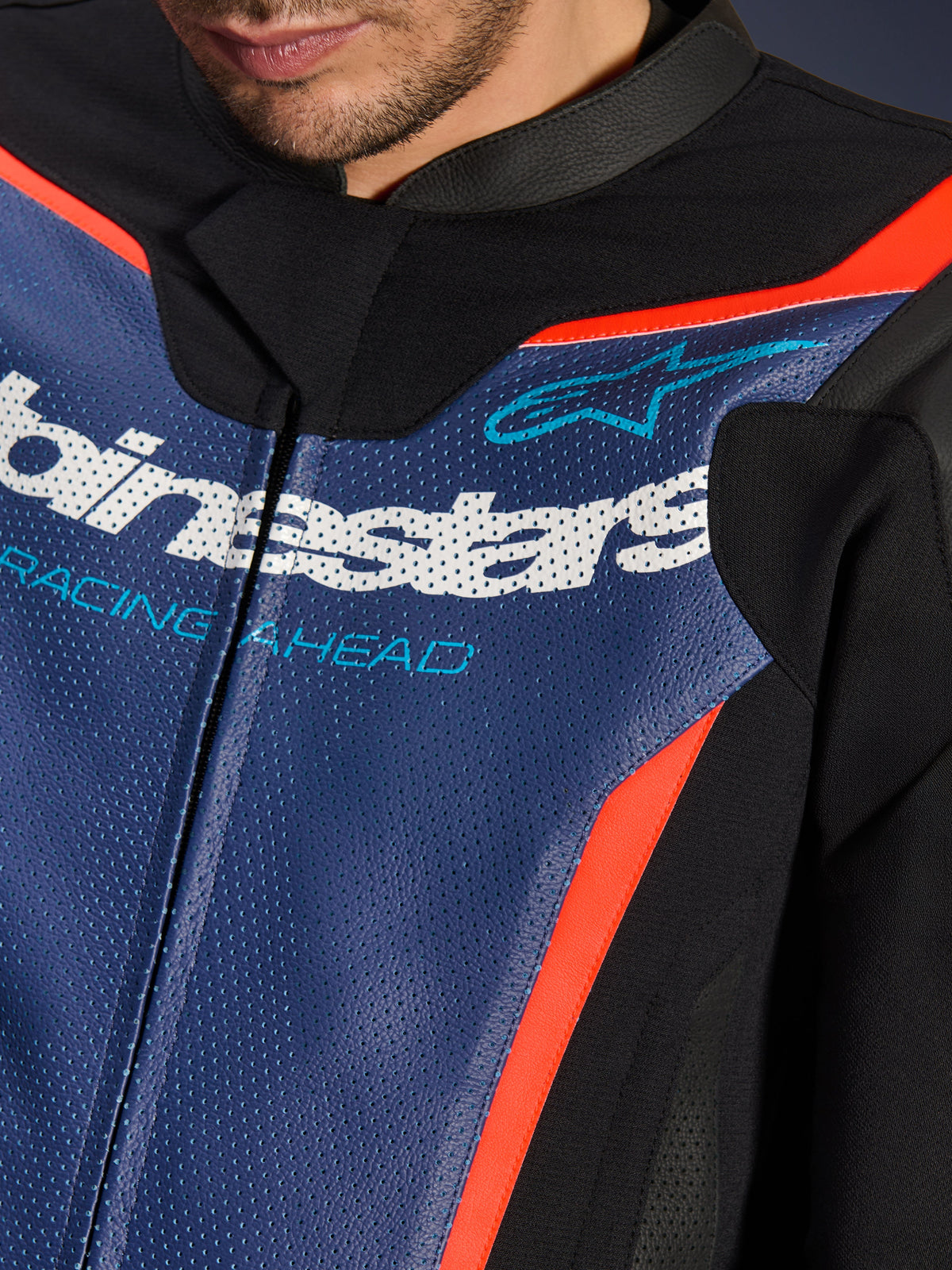 Alpinestars GP Force V2 læderdragt, 2-delt, nærbillede af brystområdet, perforeret blåt læder med hvidt logo og 'RACING AHEAD'-tekst, rød fluo-detaljer og sorte paneler, professionelt sportskøreudstyr