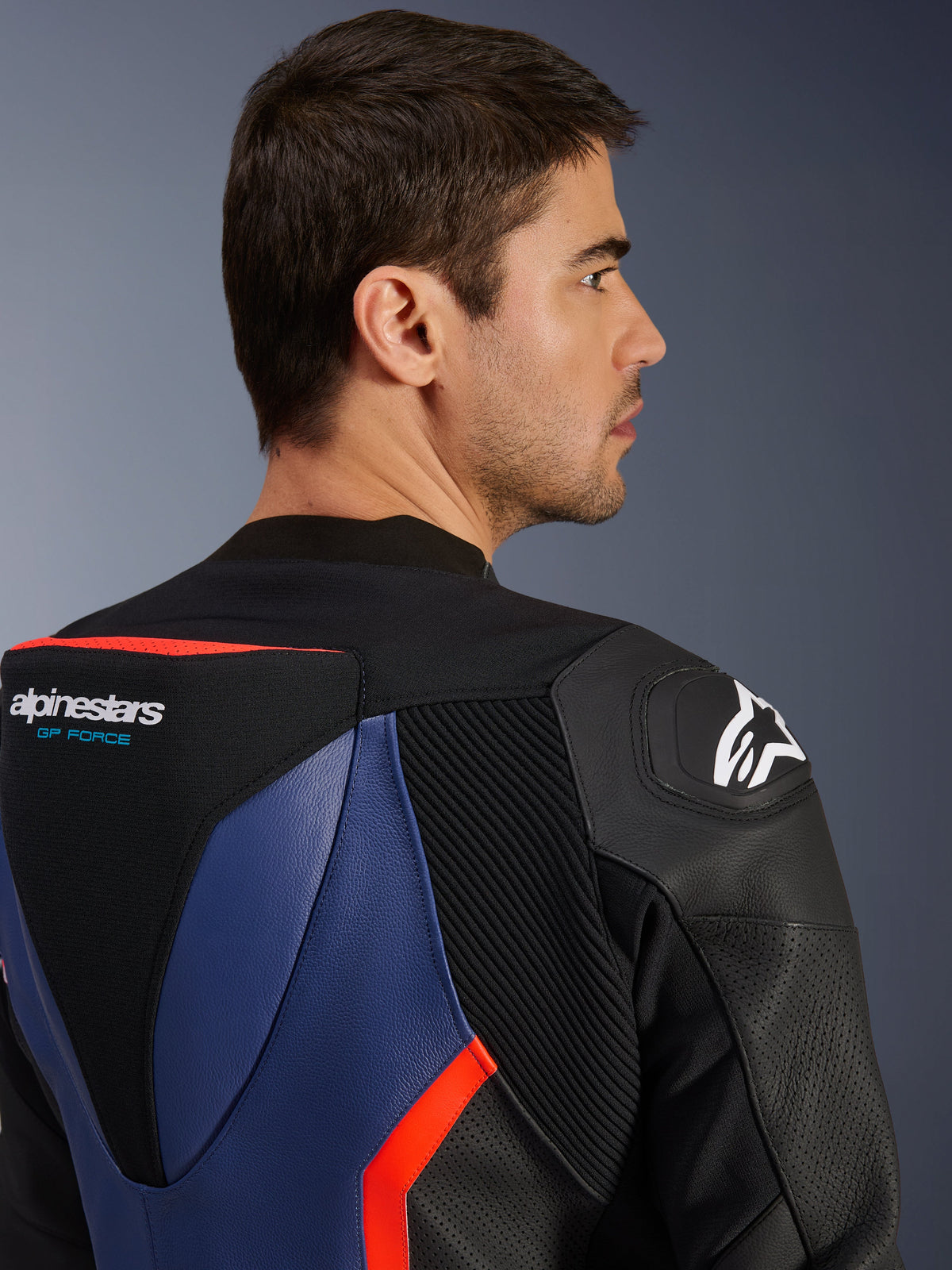 Alpinestars GP Force V2 læderdragt - 2-delt, nærbillede af øvre ryg og skulder, aerodynamisk speed hump med GP Force-logo, DFS-skulderbeskytter, sort, blå og rød fluo okselæder, perforerede paneler og harmonika-strækzoner, professionelt racerudstyr