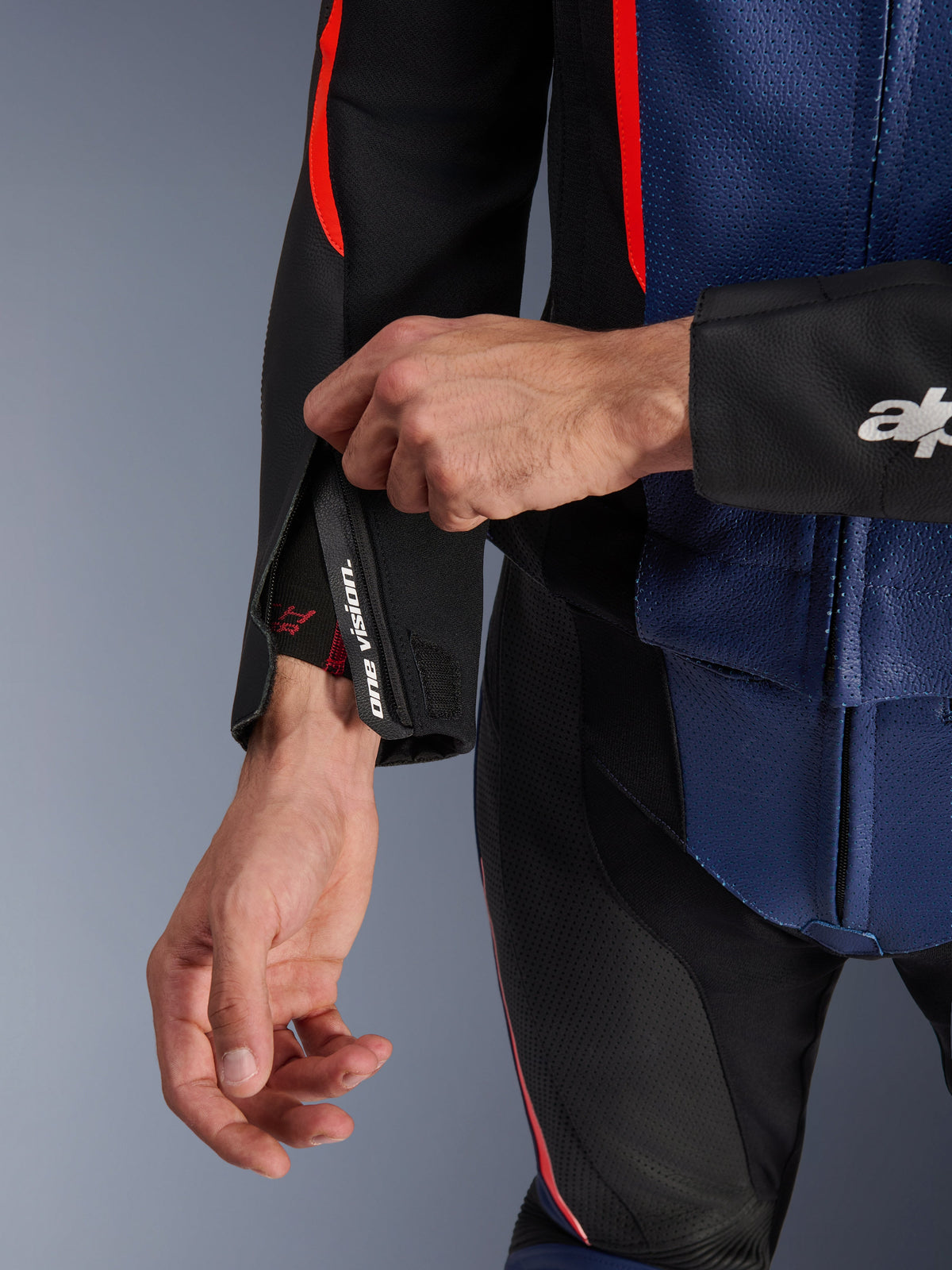 Alpinestars GP Force V2 Læderdragt- 2Piece, nærbillede af ærmemanchet og overkrop, sort, blå og rød fluo, perforeret læder, manchet med lynlås og 'one vision'-branding, fluorescerende røde accenter, professionelt sportsudstyr til motorcykelkørsel