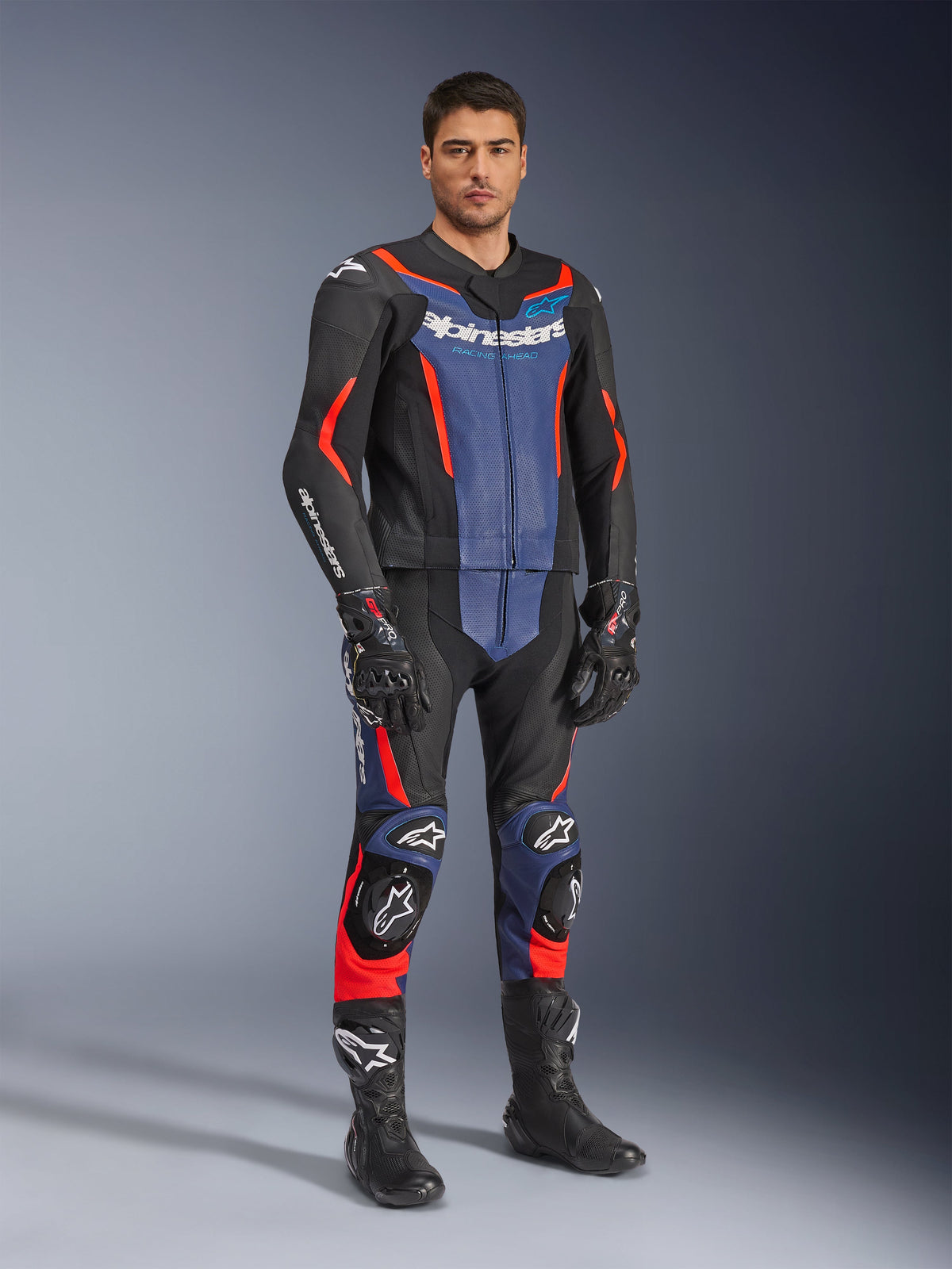Alpinestars GP Force V2 læderdragt 2-delt, motorcykellæderdragt, sort, blå og rød fluo, båret med matchende sorte racerhandsker og støvler, med perforerede paneler og beskyttende skydere, aerodynamisk design til sportskørsel