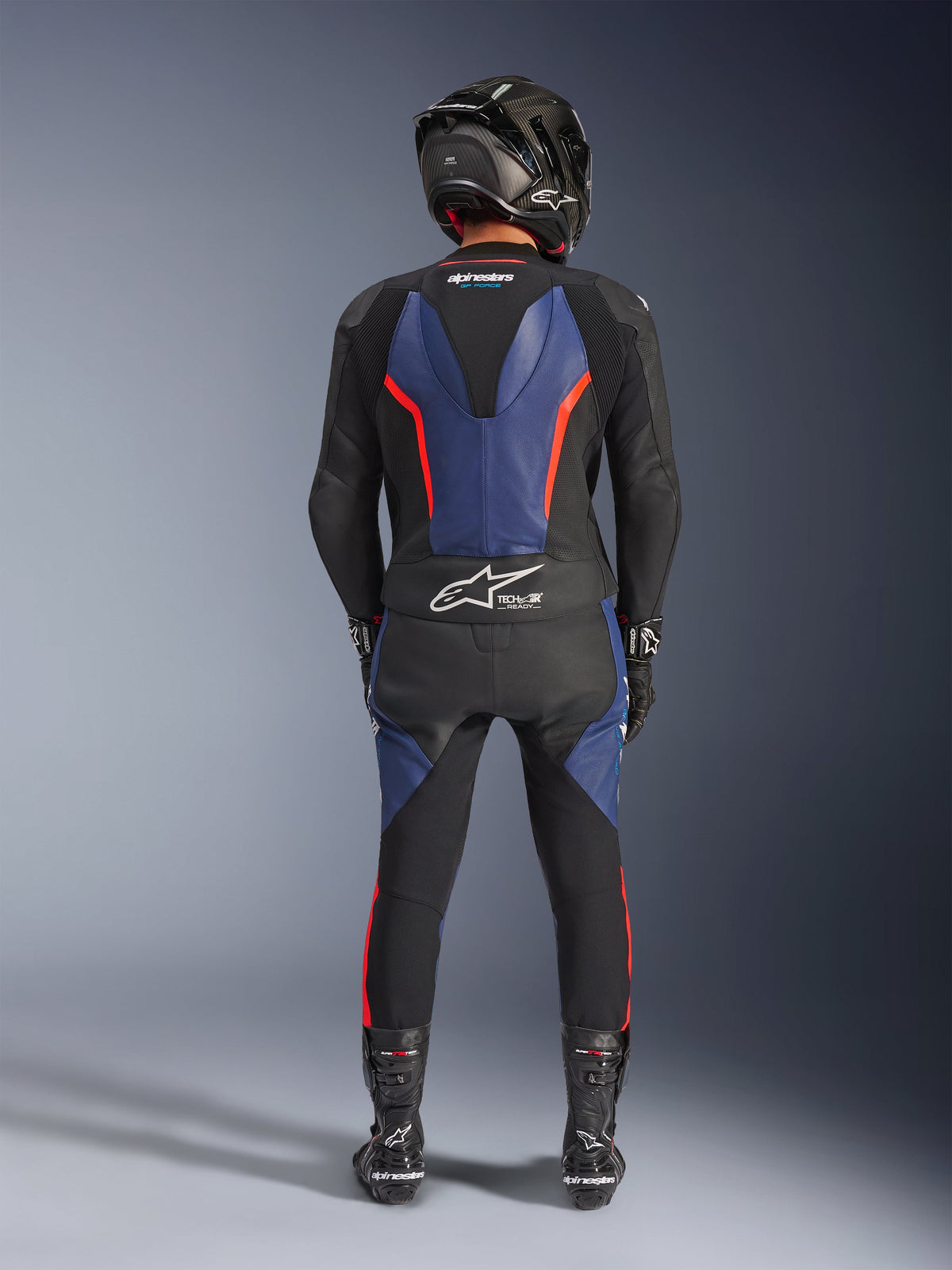 Alpinestars GP Force V2 Læderdragt 2-Piece, Black Blue Red Fluo, fuld bagfra visning af en kører i komplet racerudstyr, med blå læderpaneler på ryggen og benene med fluorescerende røde detaljer, Tech-Air® Ready-logo på den nederste del af ryggen, kombineret med en kulfiberhjelm, sorte handsker og racerstøvler.