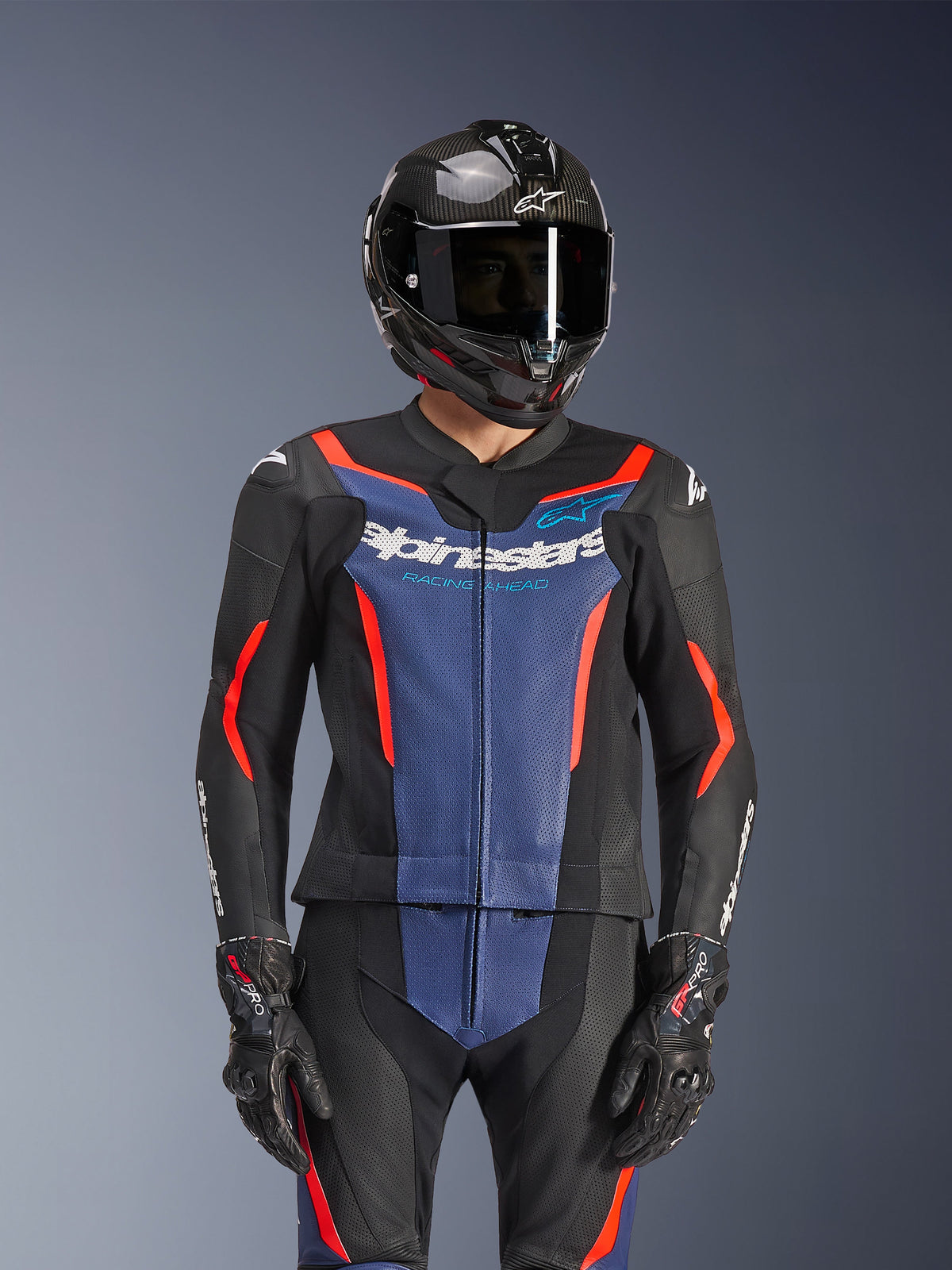 Alpinestars GP Force V2 Læderdragt 2-Piece, sort, blå og rød fluo, båret med kulfiberhjelm og racerhandsker, med perforerede læderpaneler og hvidt Alpinestars-logo på brystet, professionelt racer- og sportsudstyr