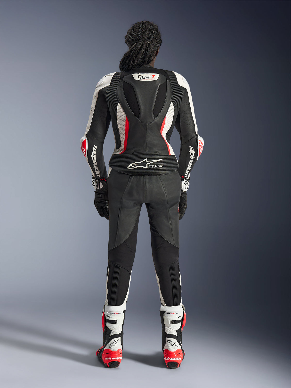 Bagsiden af Alpinestars Stella GP-R7 2-delt læderdragt, sort, hvid og rød fluo, med en aerodynamisk pukkel med GP-R7-branding og Tech-Air Ready-logo, vist med matchende racingstøvler og handsker, professionelt motorcykeludstyr til kvinder