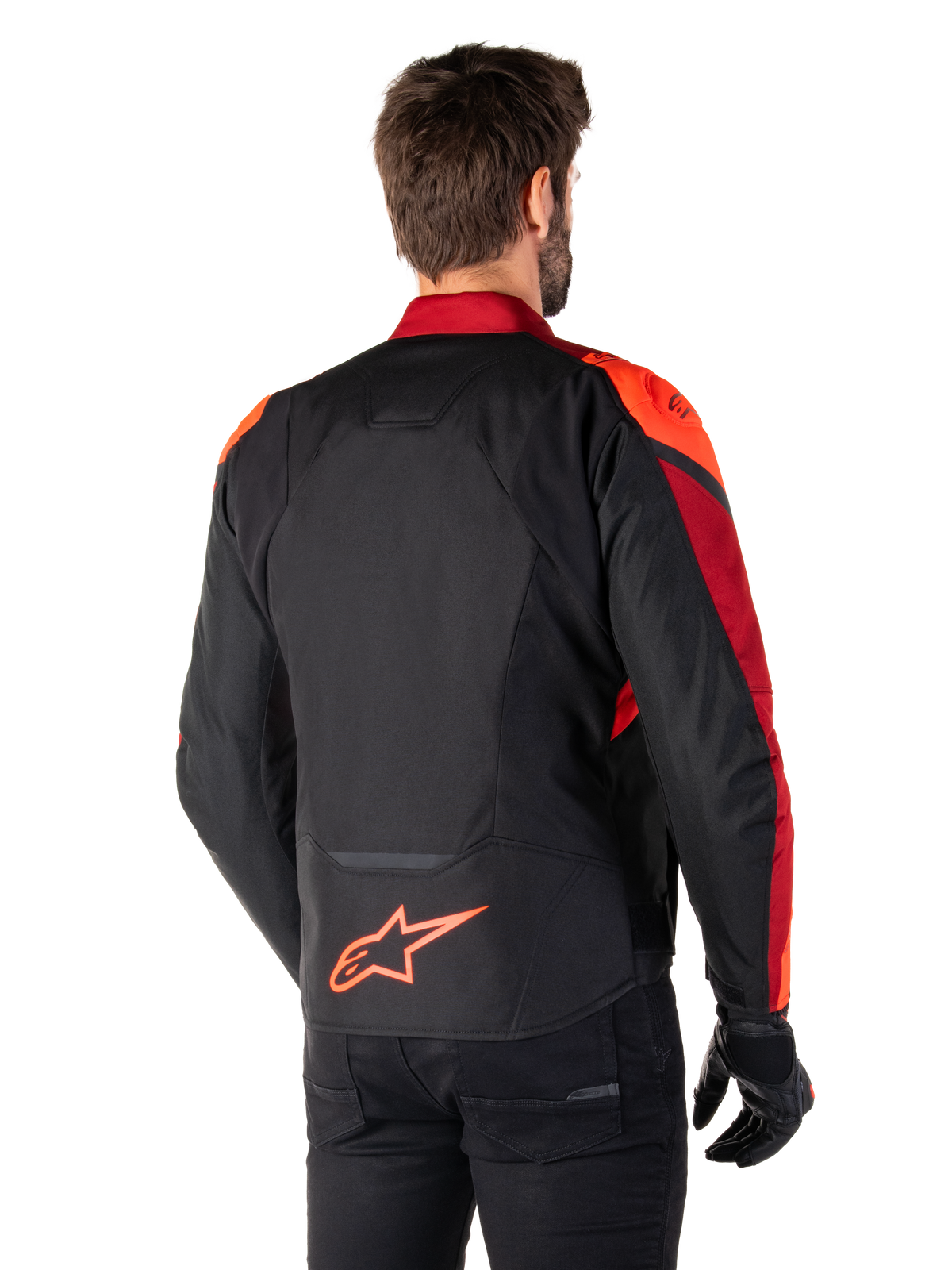 Set bagfra ses en mand iført Alpinestars T-Jaws V4 Waterproof-jakke i Black Red Fluo Dark Red, med markante røde detaljer på skuldre og ærmer, et fluorødt Alpinestars-logo på lænden, kombineret med sorte bukser og handsker.