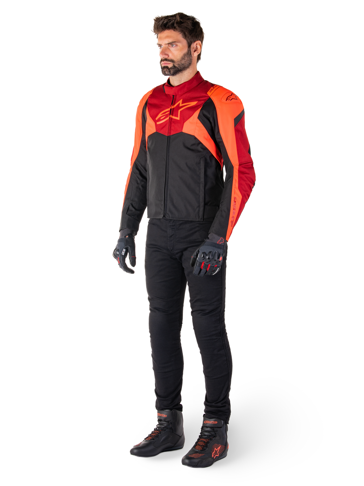 Mandlig rytter iført Alpinestars T-Jaws V4 vandtæt jakke i Sort Rød Fluo Mørkerød, kombineret med sorte motorcykelbukser, handsker og kørestøvler, sport-fit tekstildesign med markant logo på brystet og en aggressiv silhuet.
