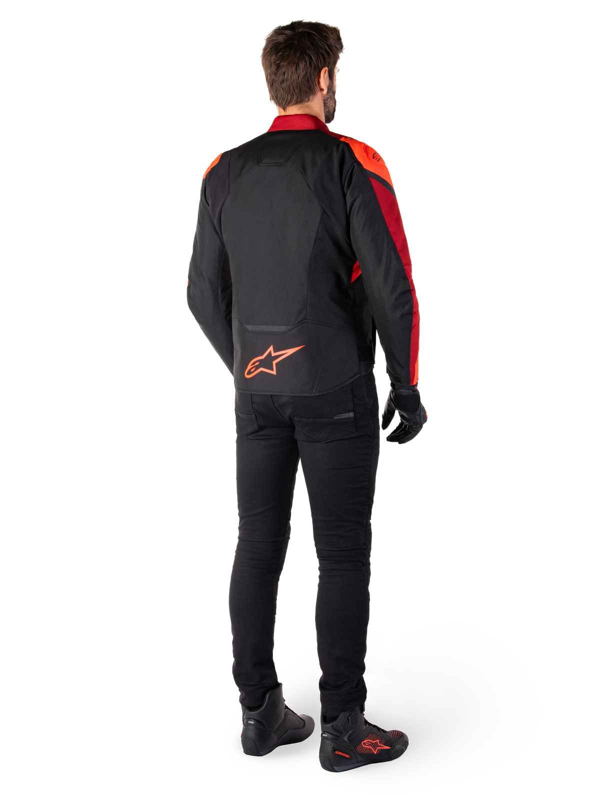 Alpinestars T-Jaws V4 vandtæt jakke i sort, rød fluo og mørkerød, set bagfra på en kører iført tekstiljakken med sorte bukser og kørselstøvler, med et markant rødt Alpinestars-logo nederst på ryggen.